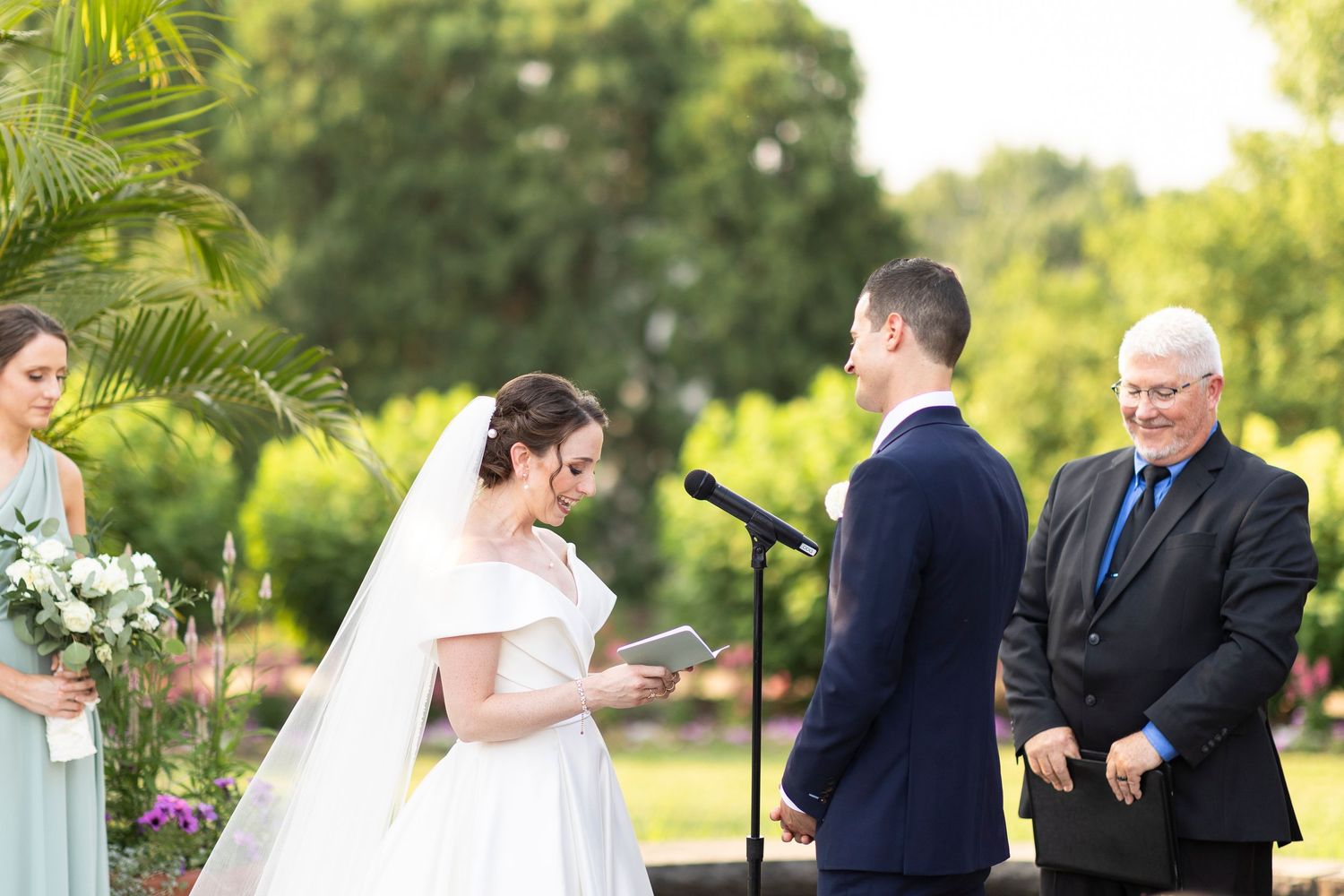 Wedding ceremony in progress with couple reading vows in front of officiant in garden setting.