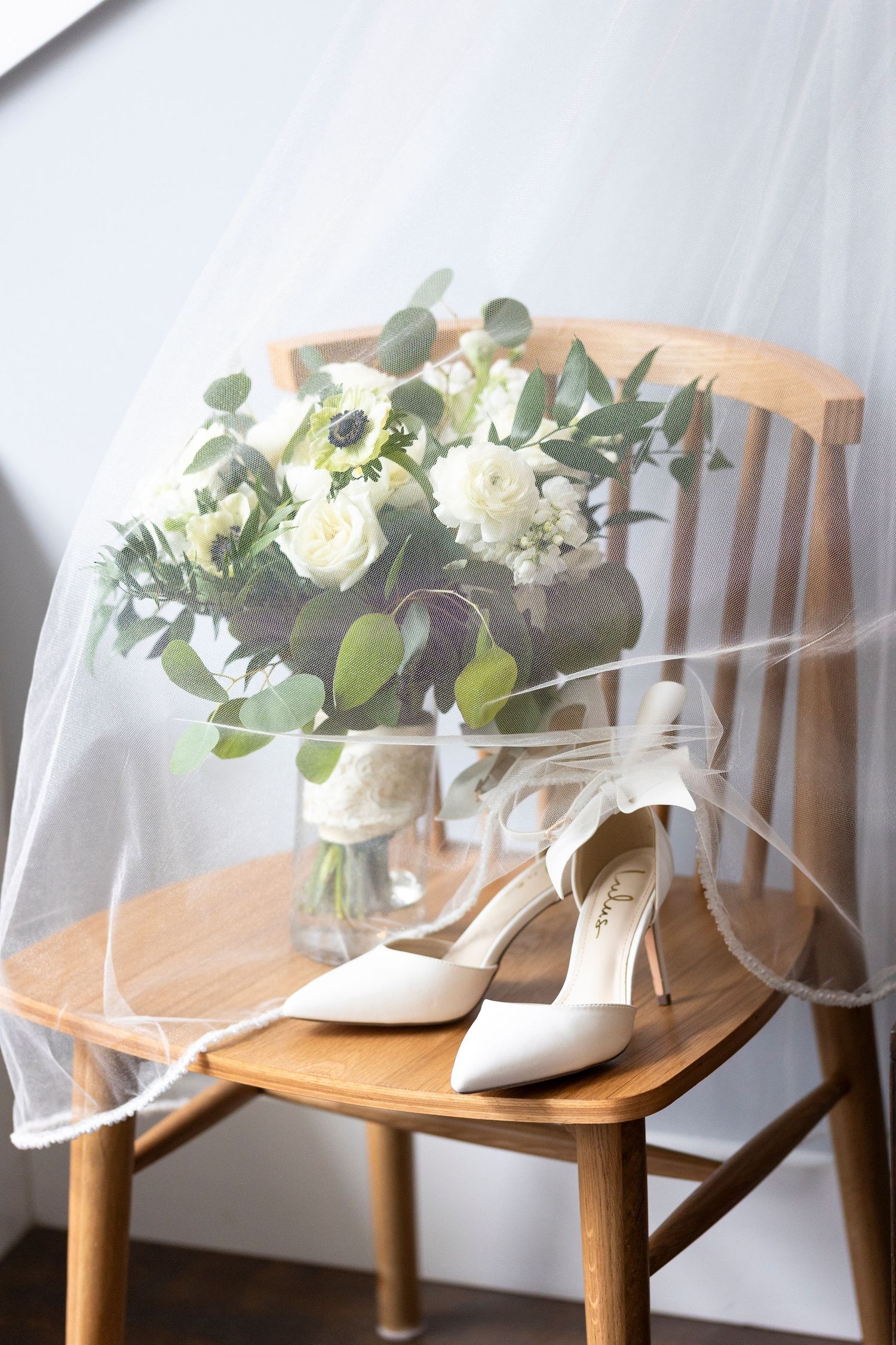 Wedding accessories including white shoes and floral arrangements displayed on wooden chairs.