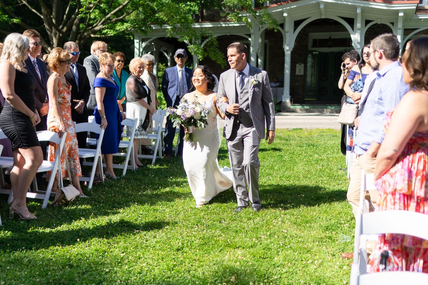 Wedding guests gather on a green lawn during an outdoor summer ceremony.