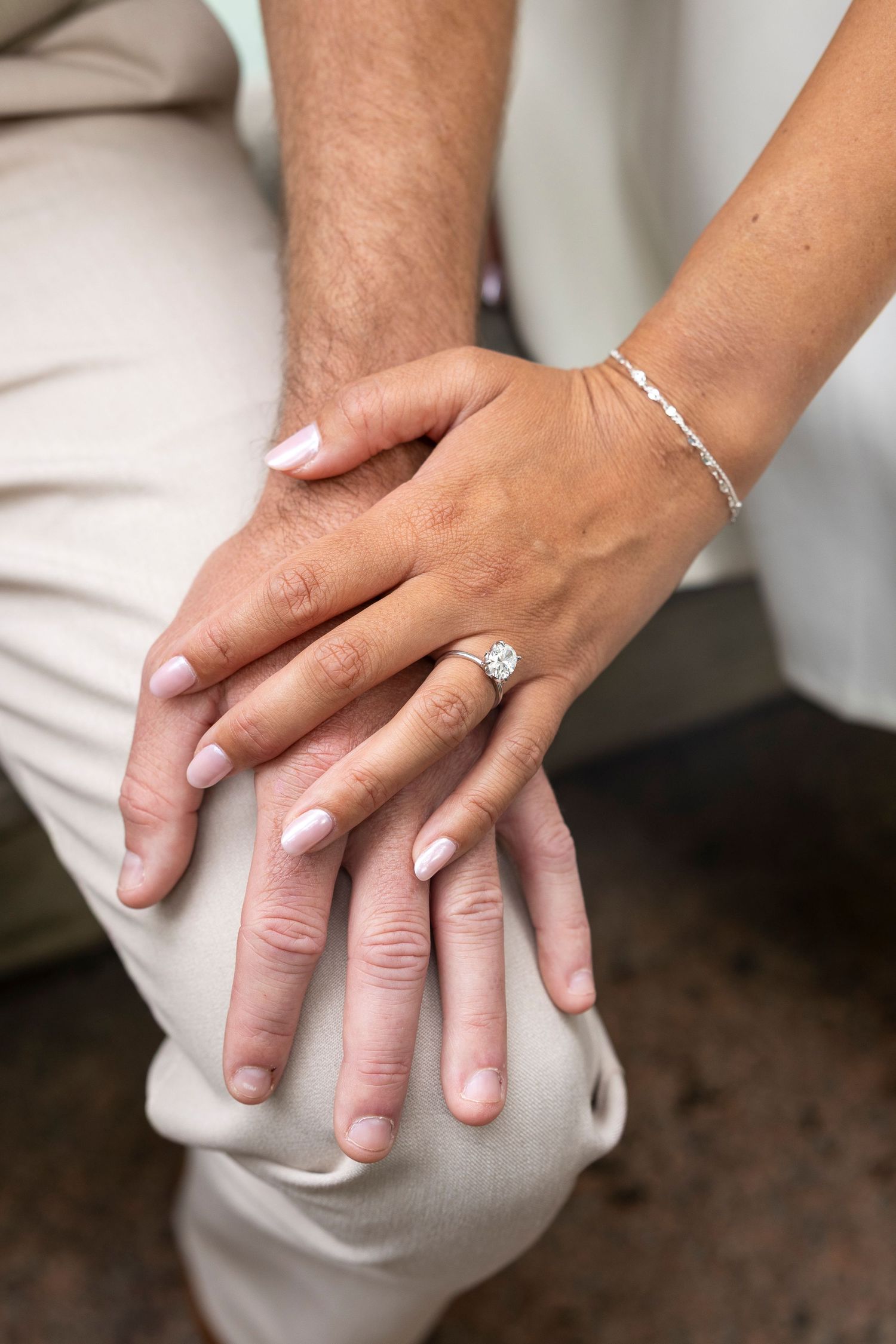 Close-up of hands with engagement ring and wedding bands resting together.