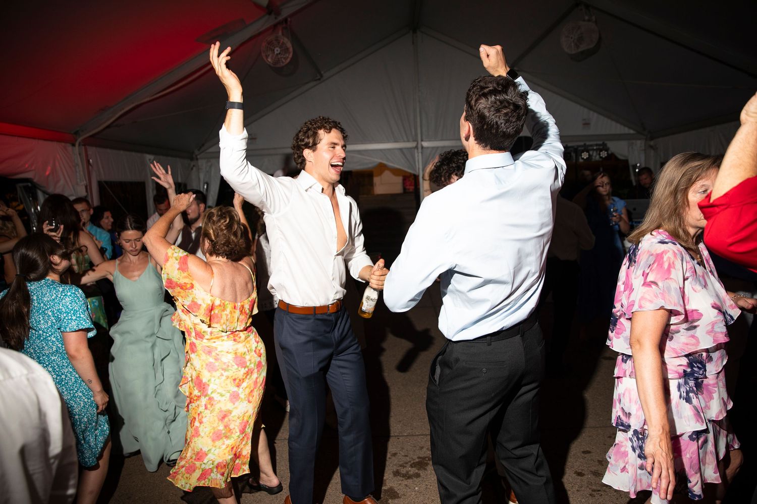 Wedding party guests dancing and celebrating under dramatic red lighting.