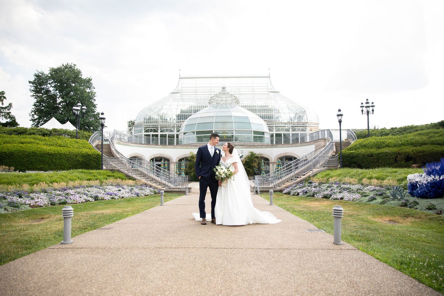 Wedding couple poses at a scenic outdoor venue with stone amphitheater and green landscape.