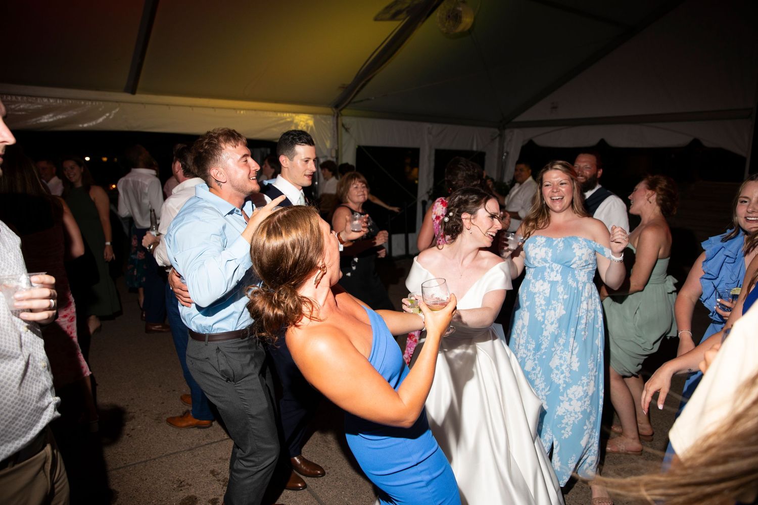Wedding celebration with guests dancing in a dimly lit tent venue.