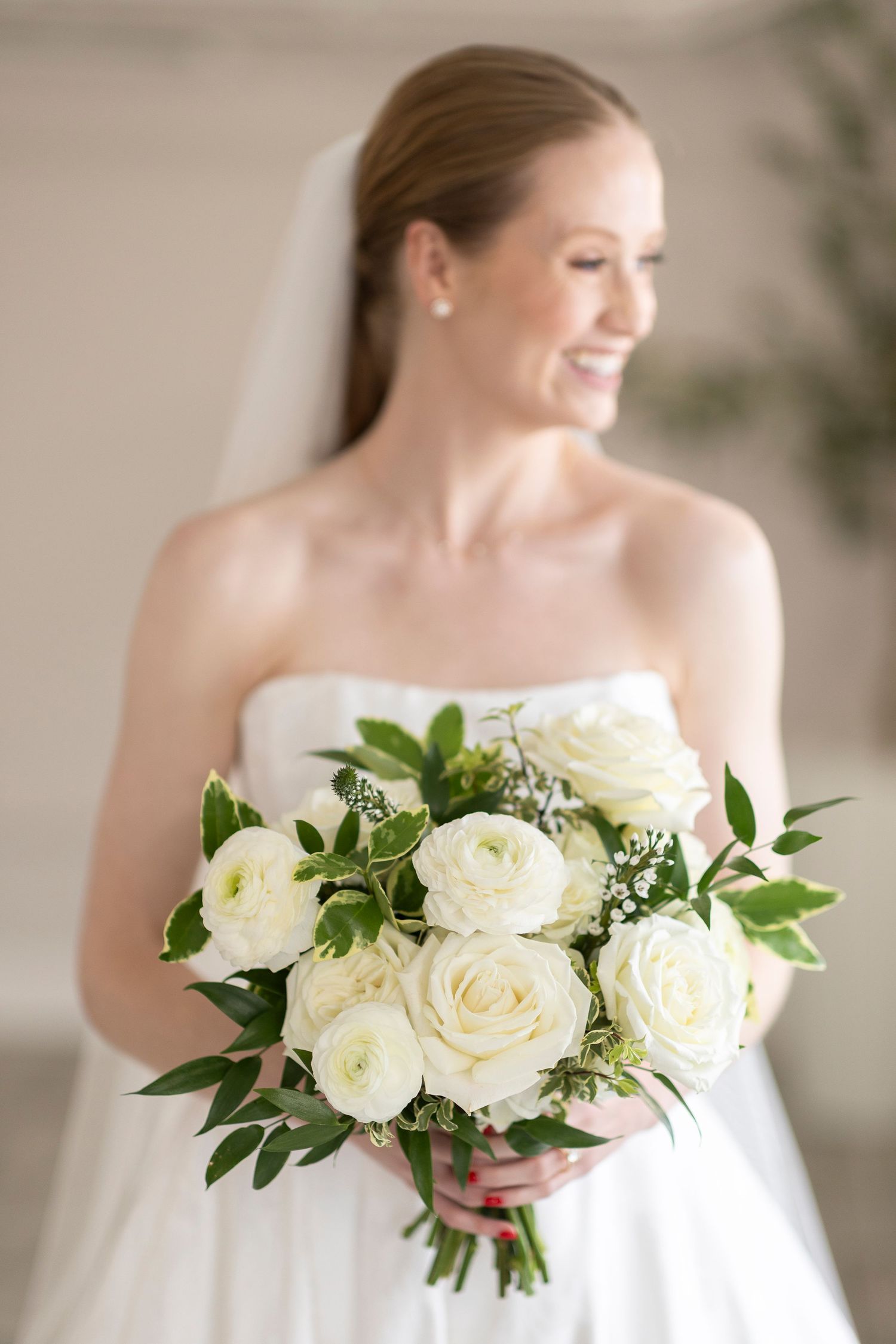 White rose bridal bouquet with green foliage held against classic wedding gown.