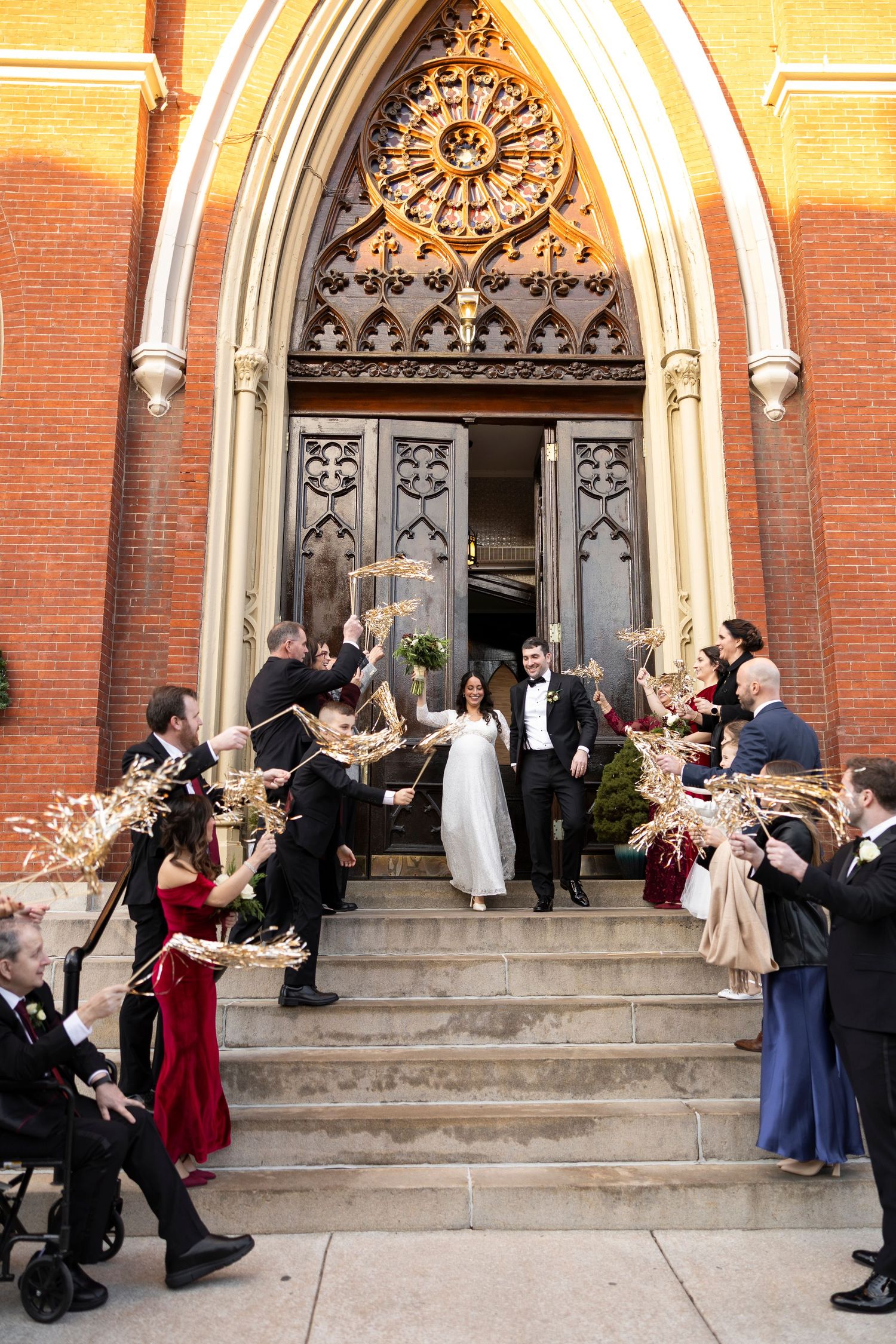 Bride and groom exit Gothic church doors as guests celebrate with dried floral arrangements on stone steps.