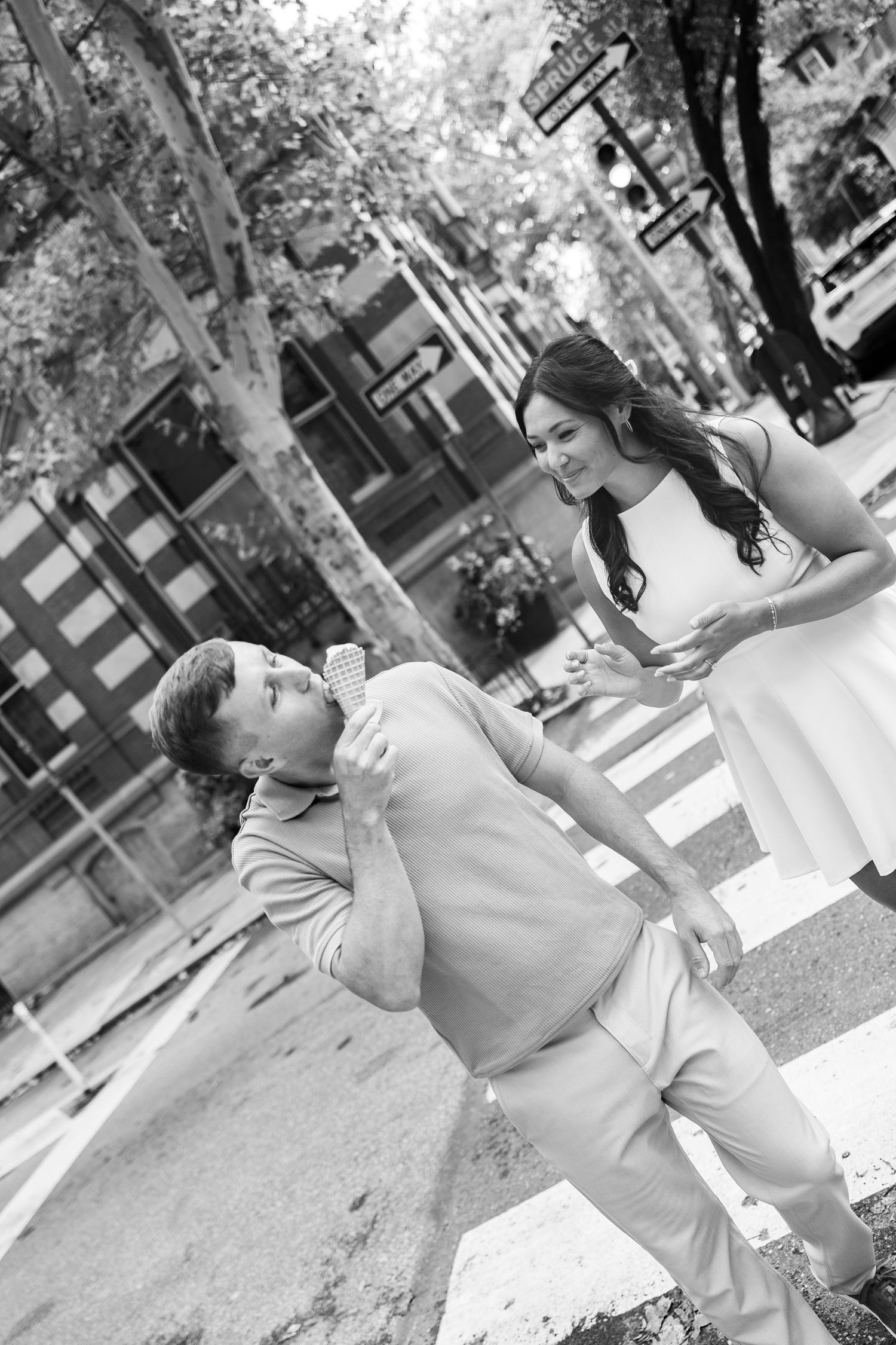 A couple shares a romantic moment on a city sidewalk in black and white photography.