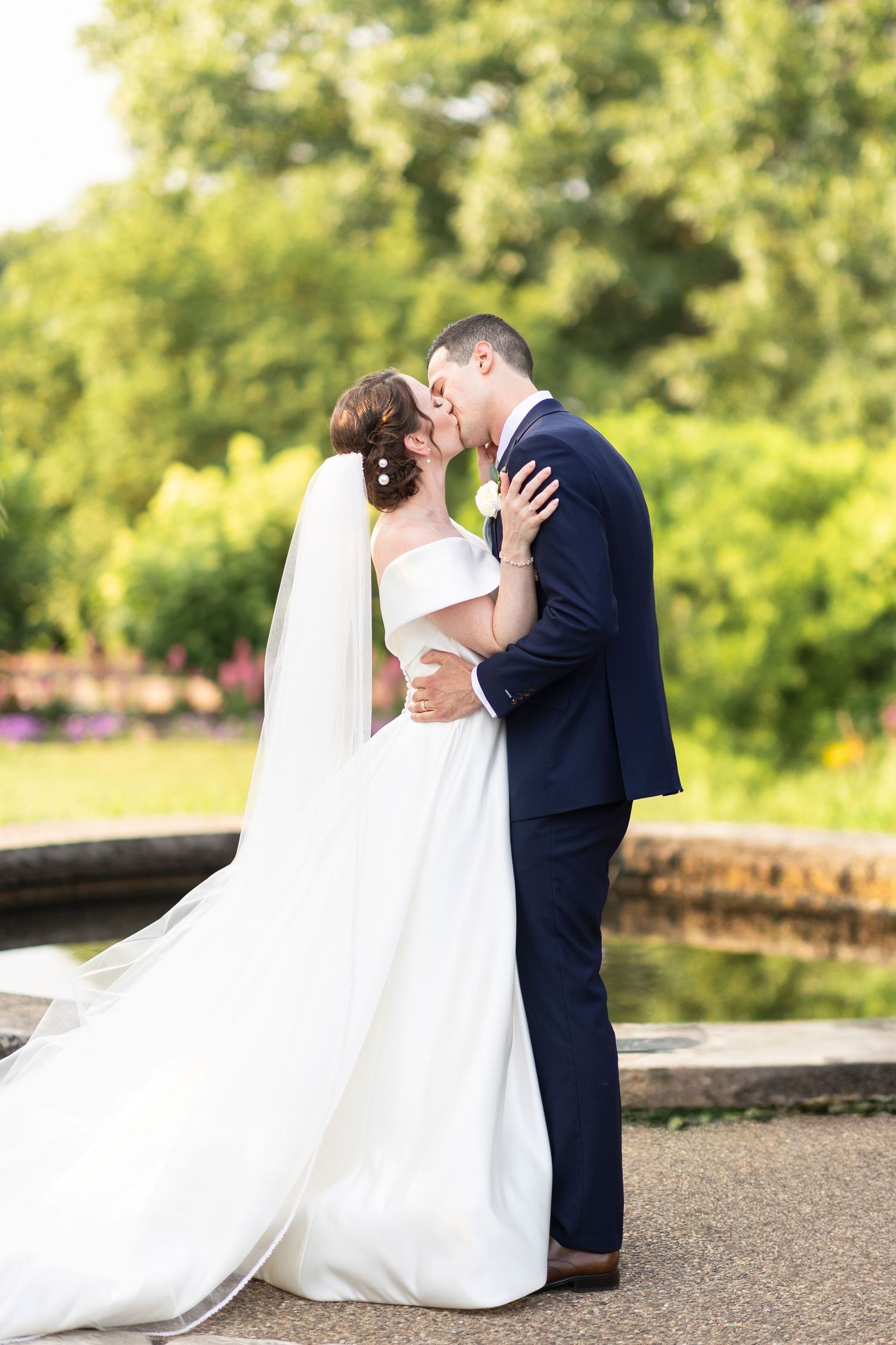 Romantic wedding portrait of newlyweds embracing on stone path in garden setting.