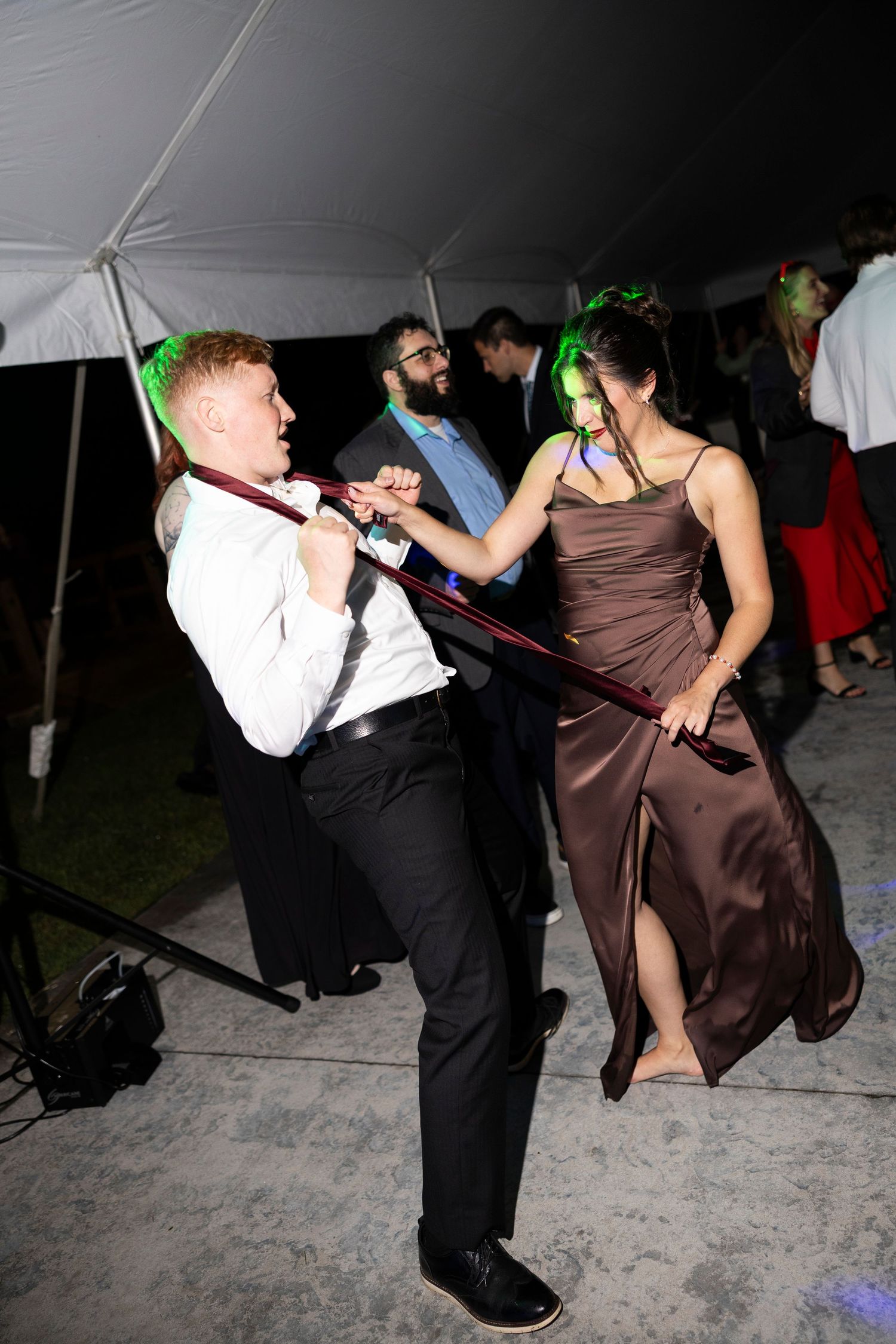 Wedding guests dancing energetically at reception under tent lighting.