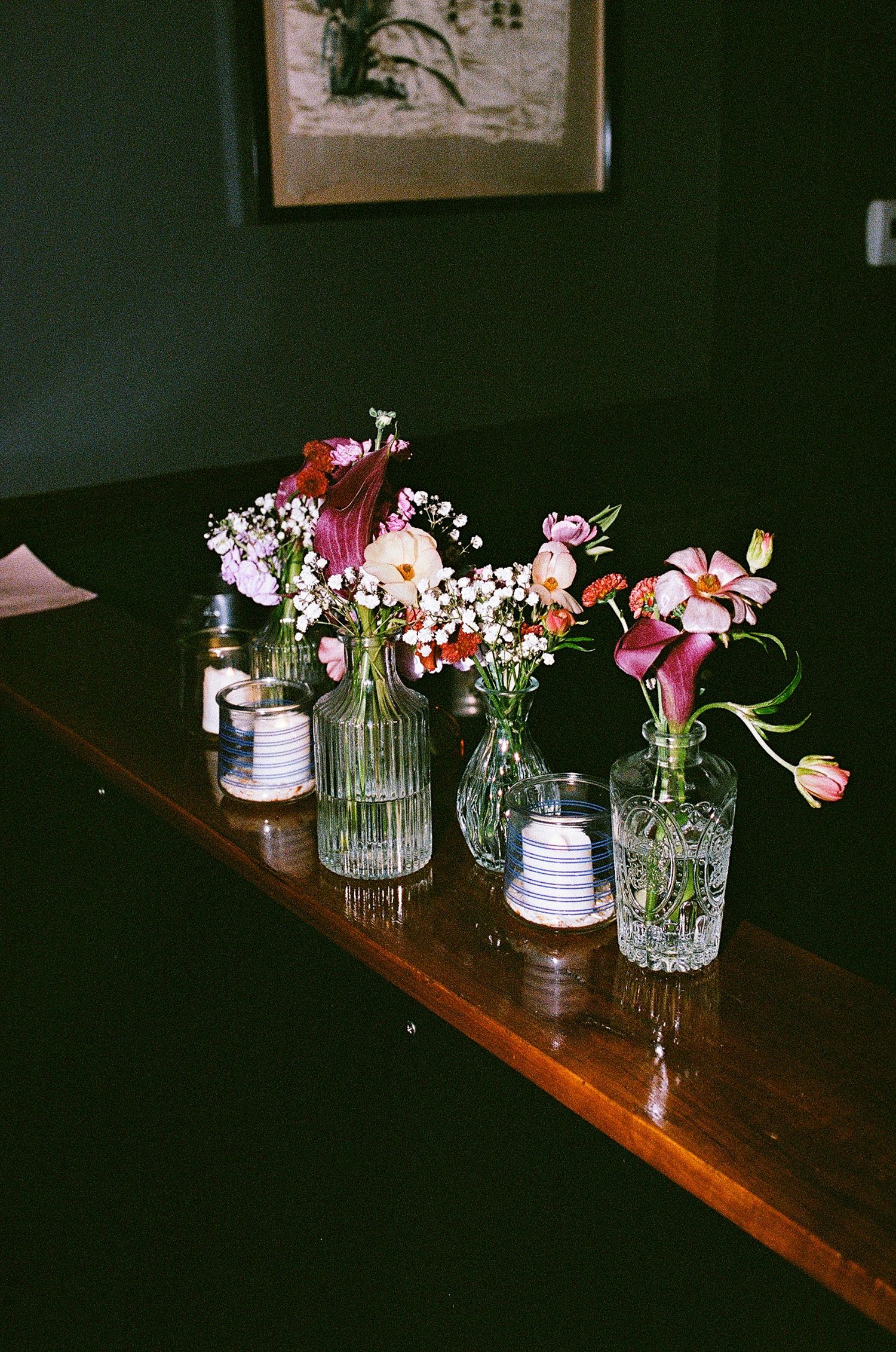 Small glass vases filled with pink and white flowers arranged on a dark wooden table.