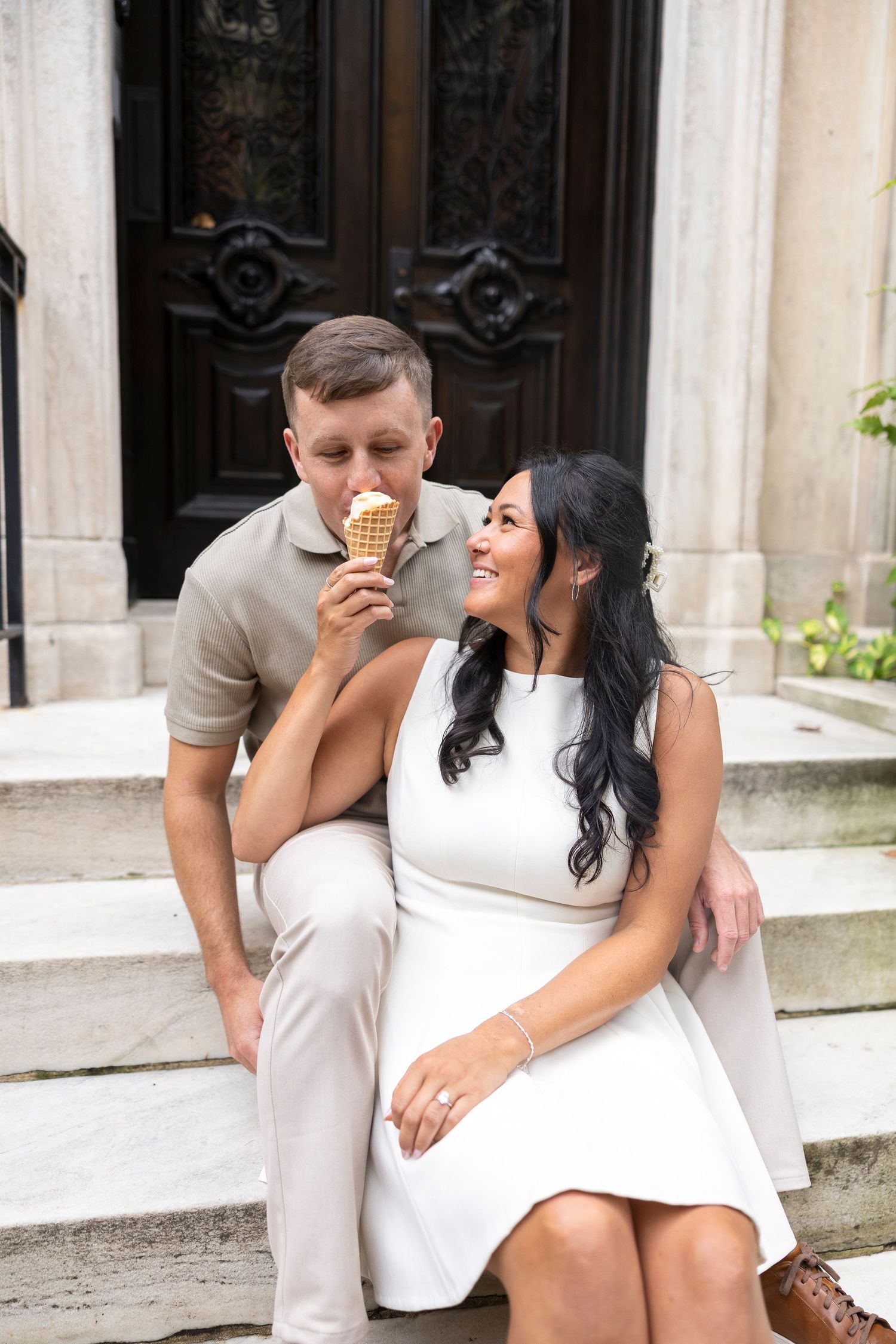A couple enjoys ice cream cones while sitting on architectural steps in casual attire.