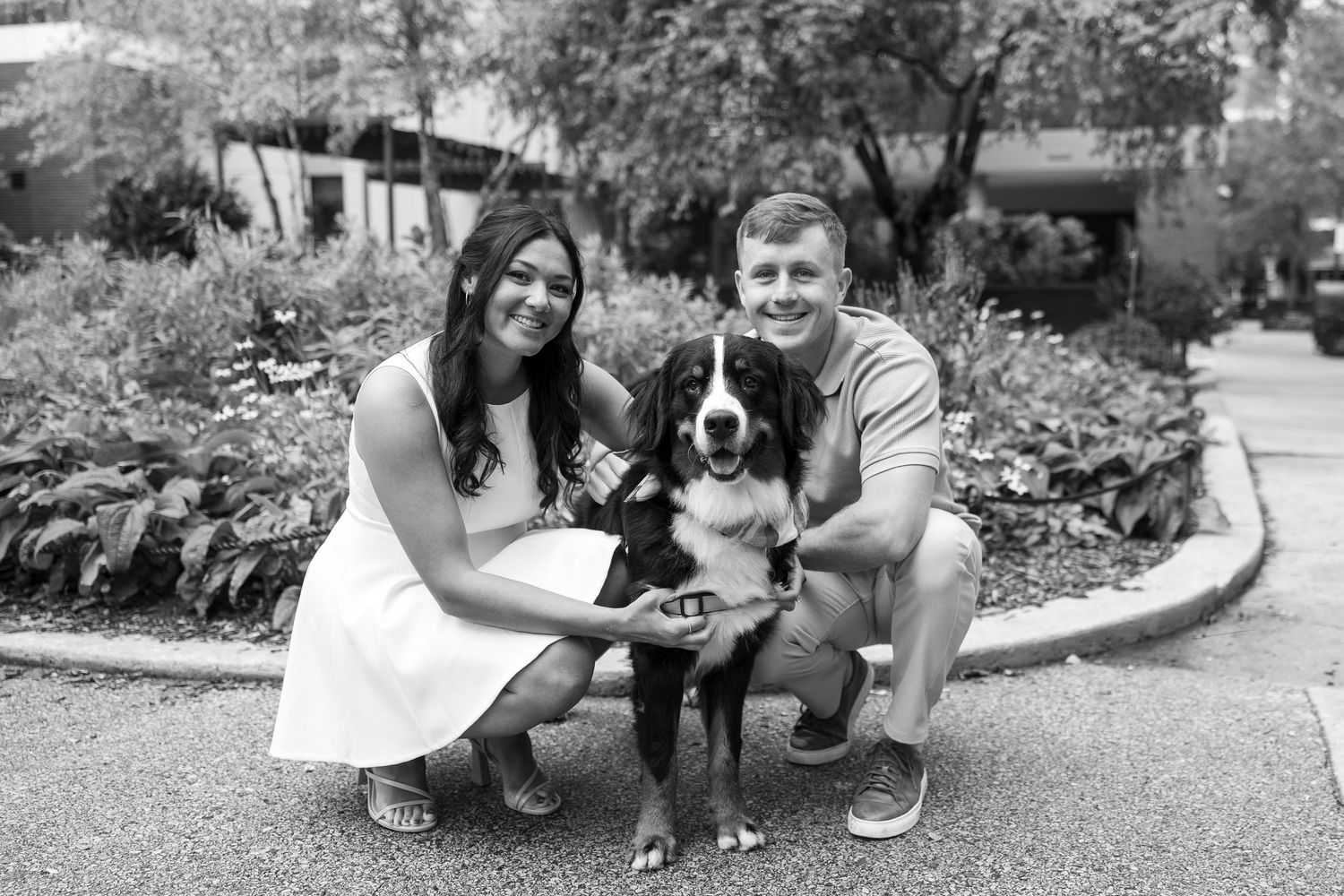 Black and white photo of a couple with their dog during an outdoor photoshoot.