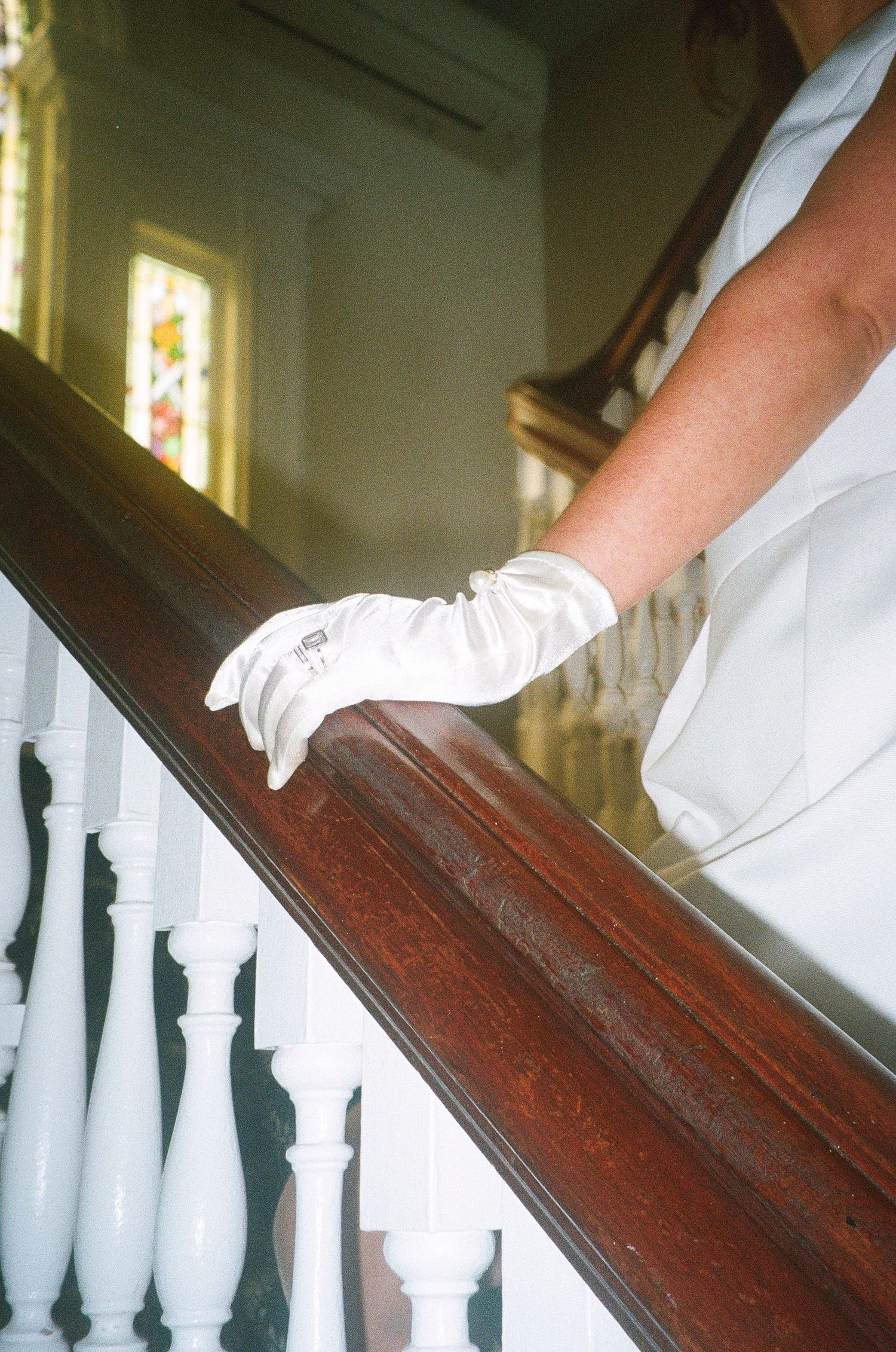 Close-up detail of a white gloved hand sliding down a wooden banister.