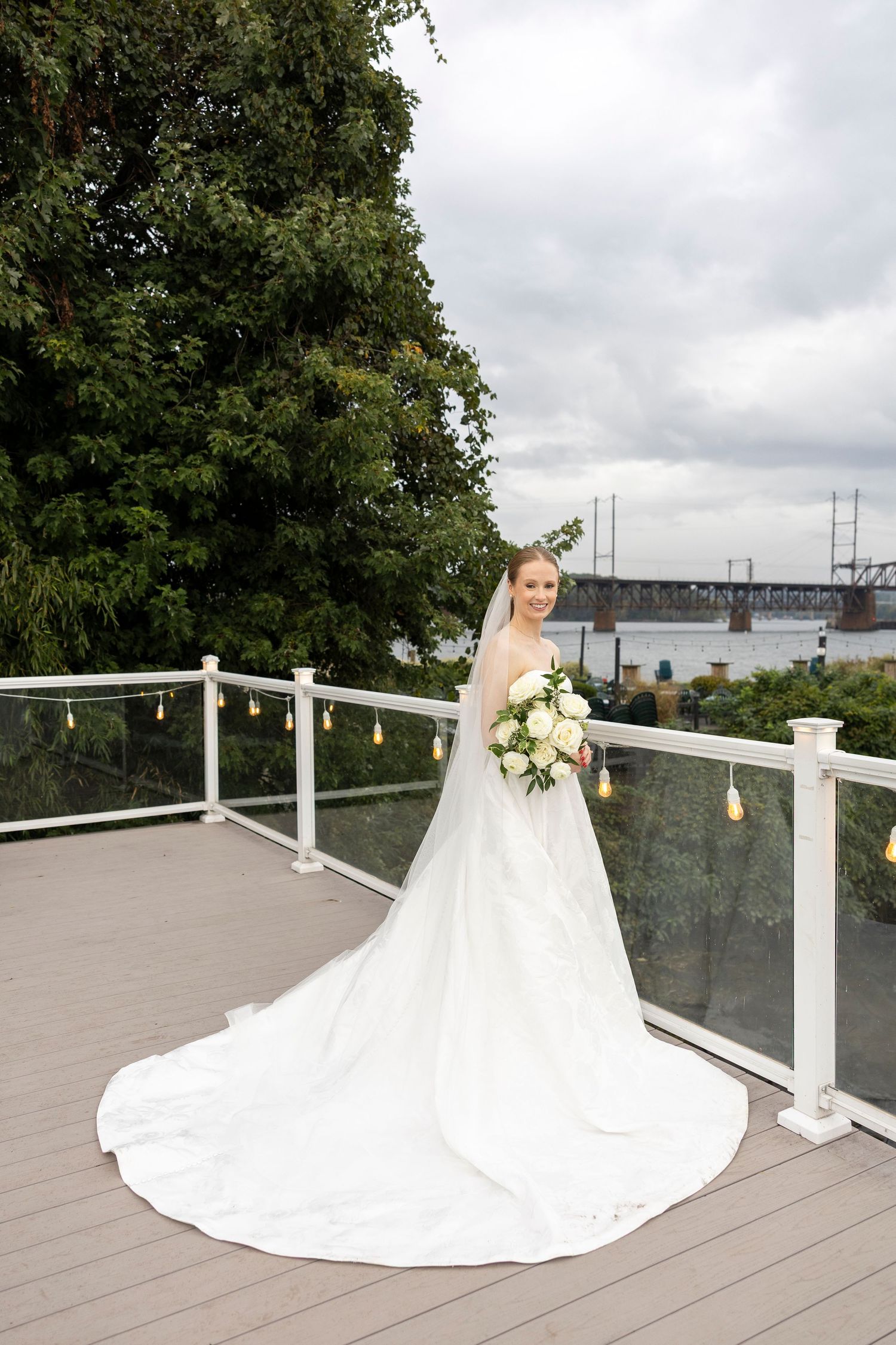 A bride in a flowing white gown poses on a waterfront deck with decorative lanterns.