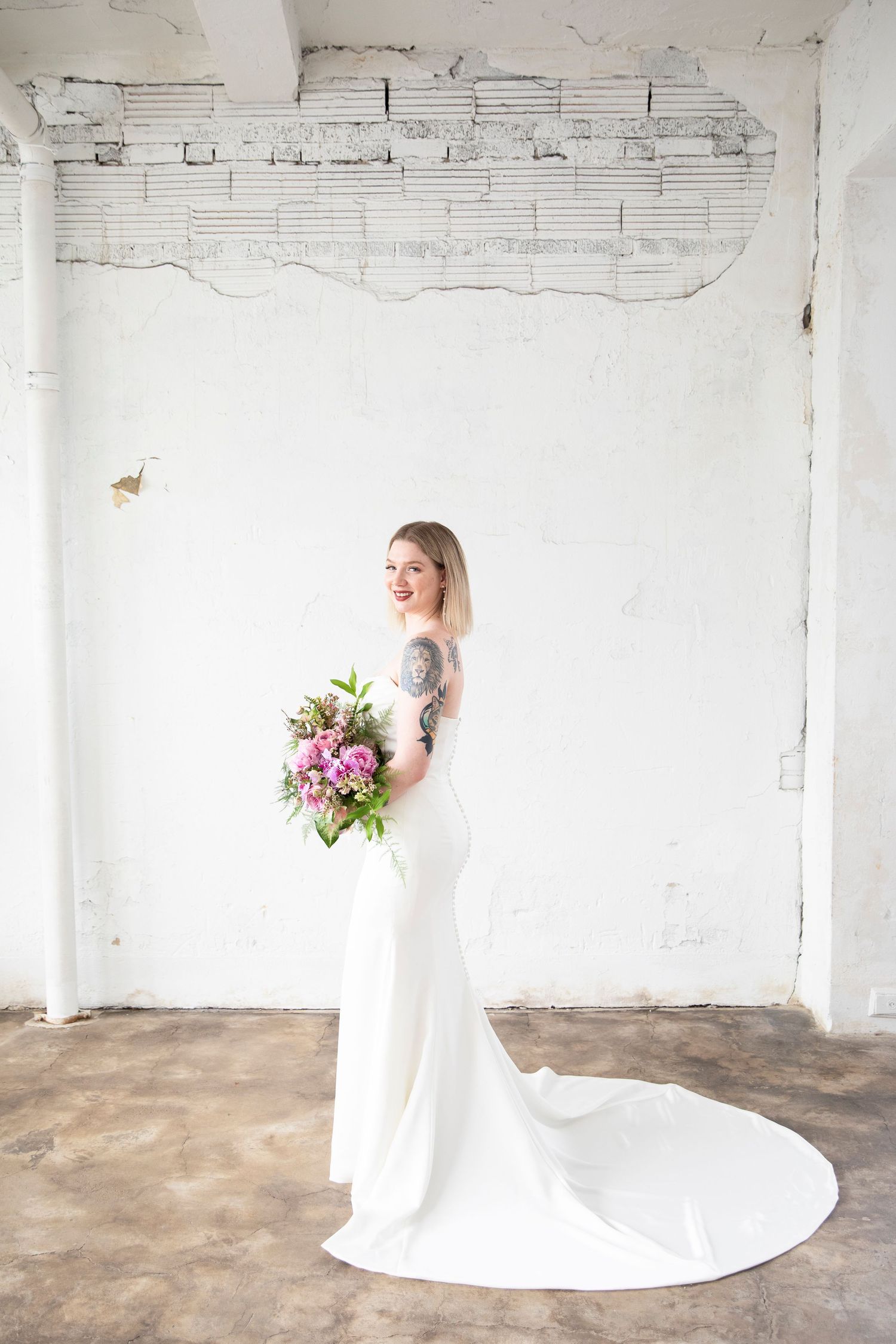 Bridal portraits with pink bouquet against white industrial backdrop.