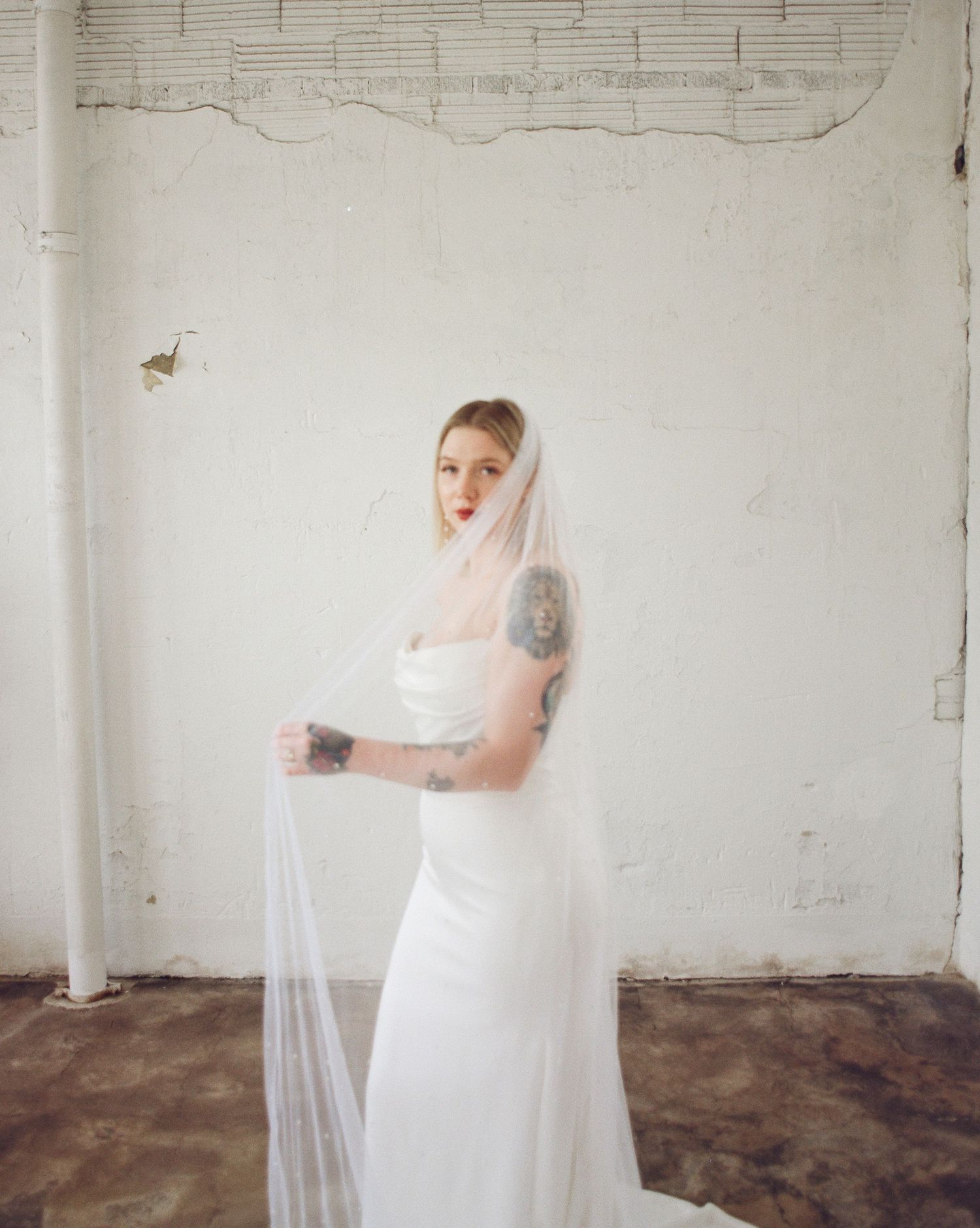Ethereal bridal portrait with flowing veil in bright white industrial space.