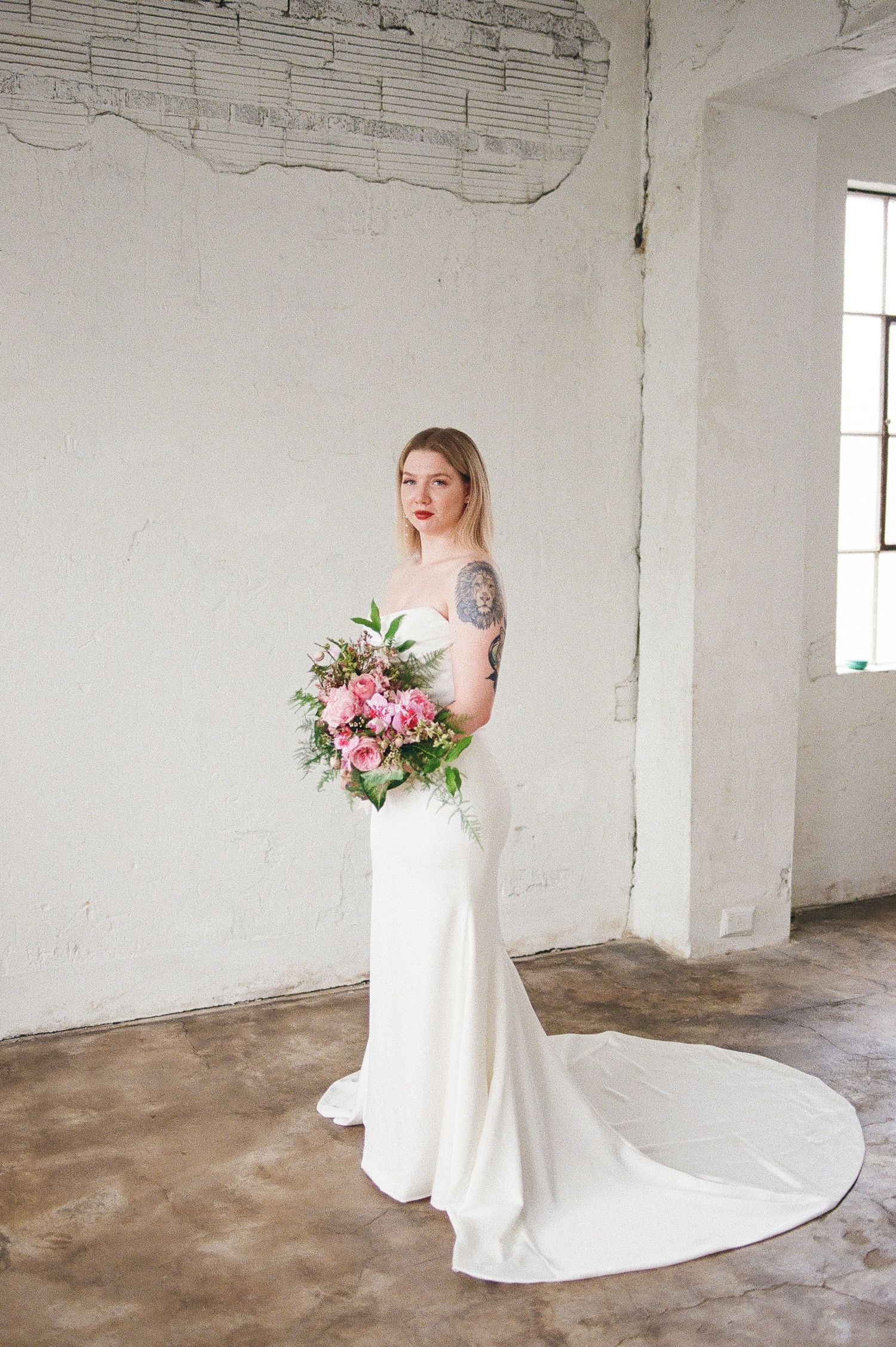 Modern bridal portraits with pink floral bouquet in white industrial space.