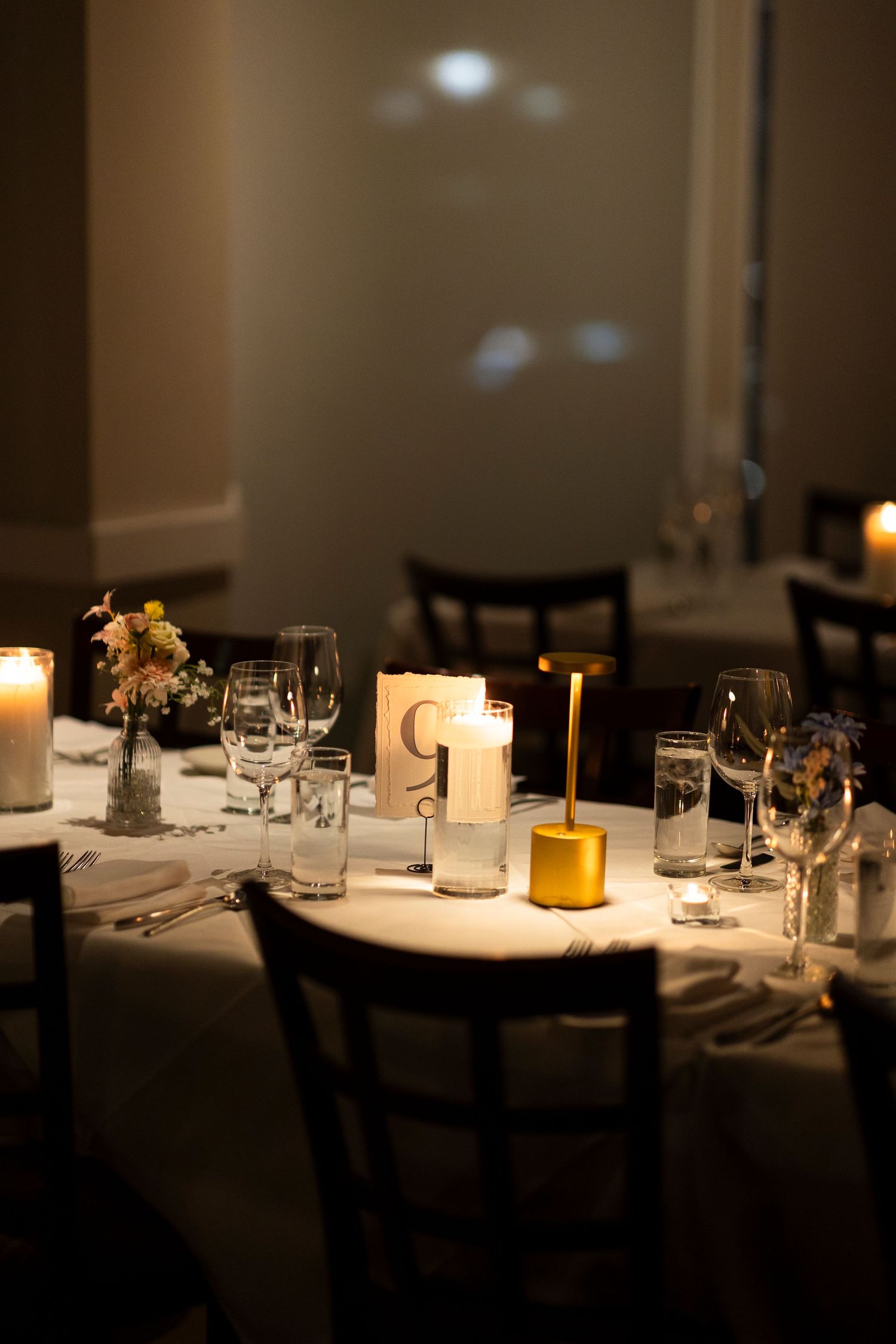 Elegant dining table set with candles and place settings in moody lighting.