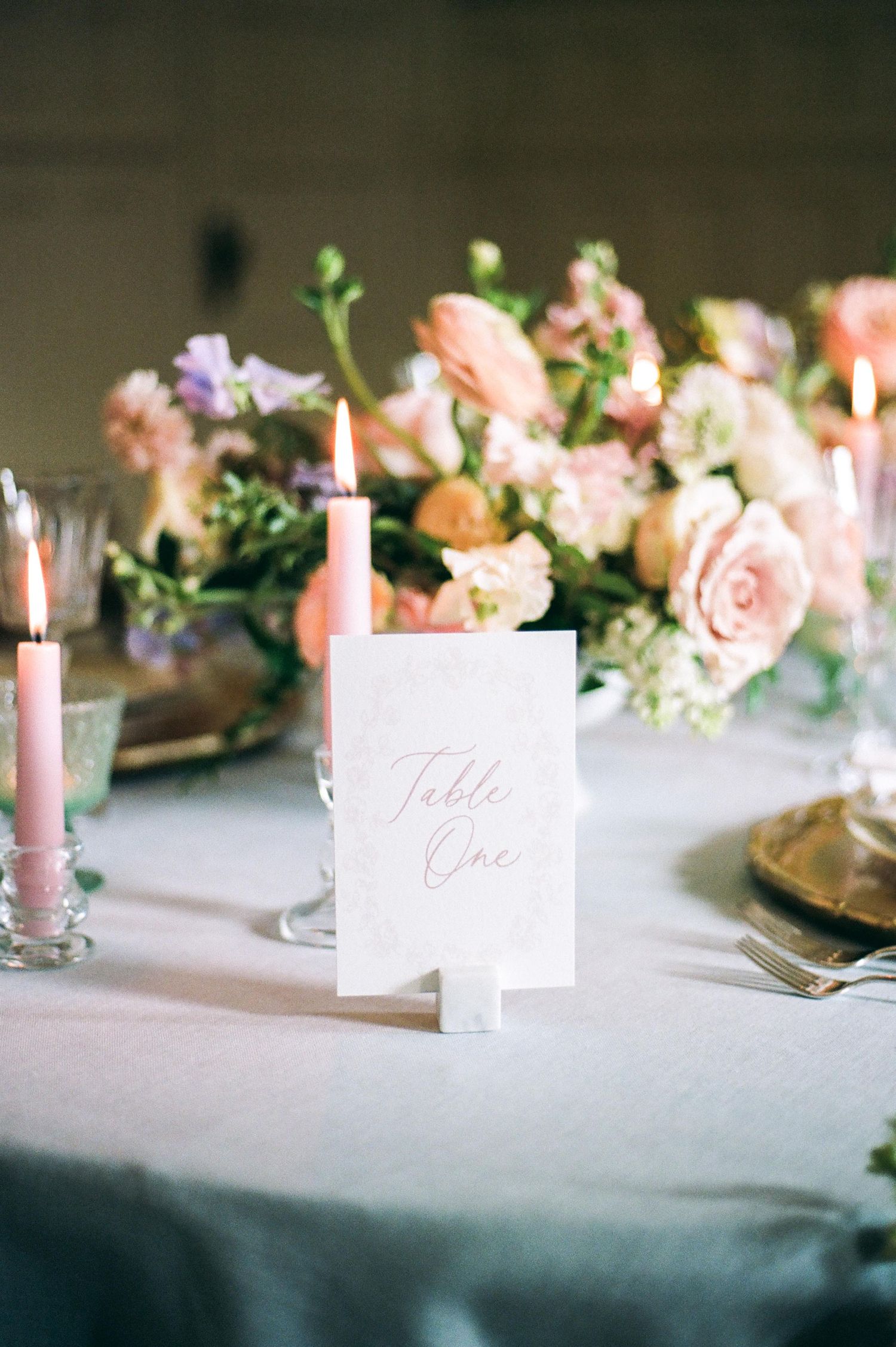 Elegant table setting with pink floral centerpieces, candles, and place cards.