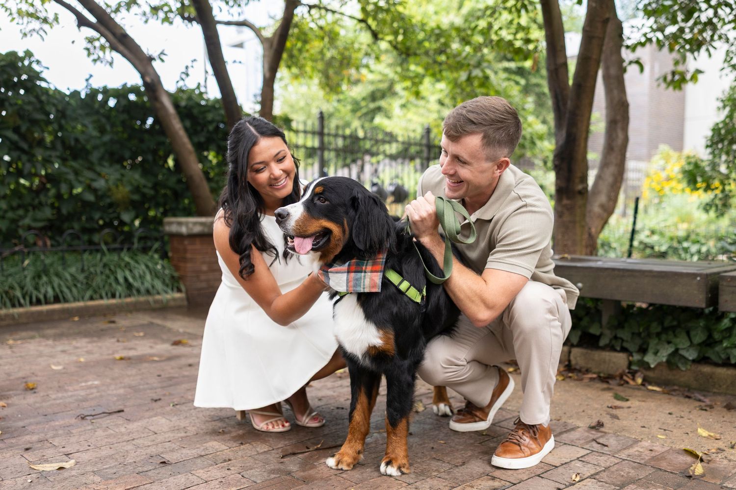 A couple poses with their Bernese Mountain Dog in a park setting during a photo session.