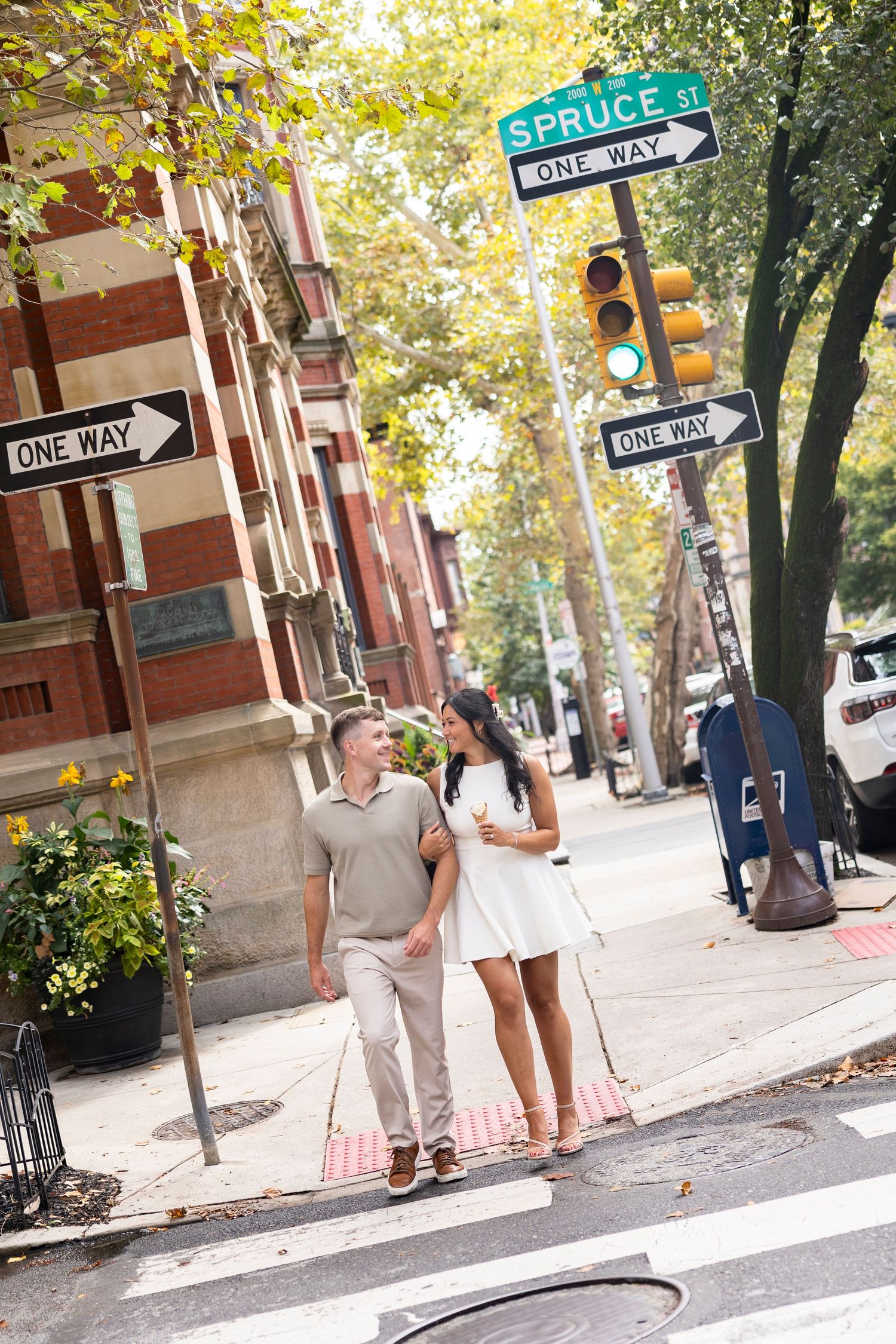 A couple walks down a tree-lined street with Spruce Street sign visible in Philadelphia.