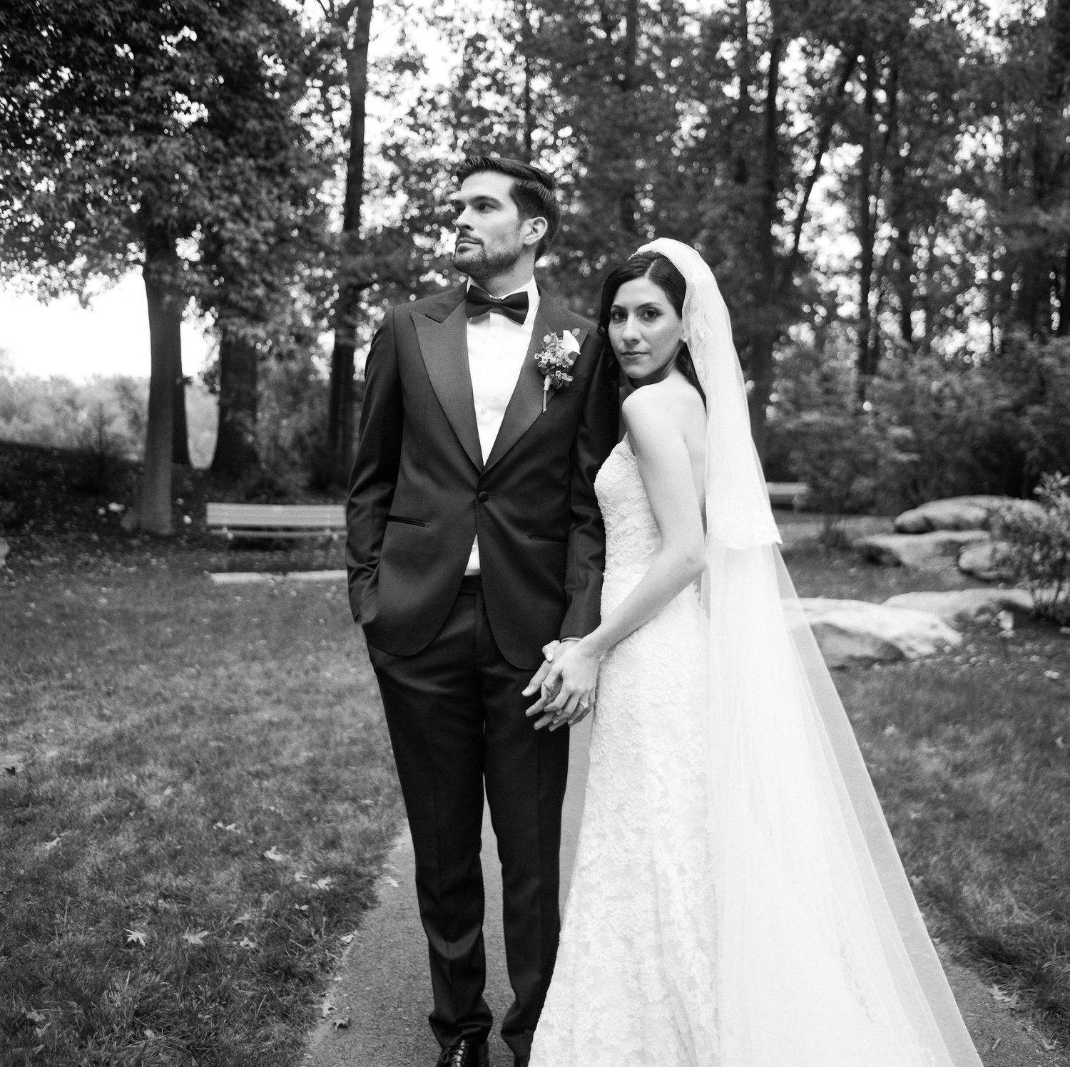 A wedding couple walks together on a garden path in formal attire.