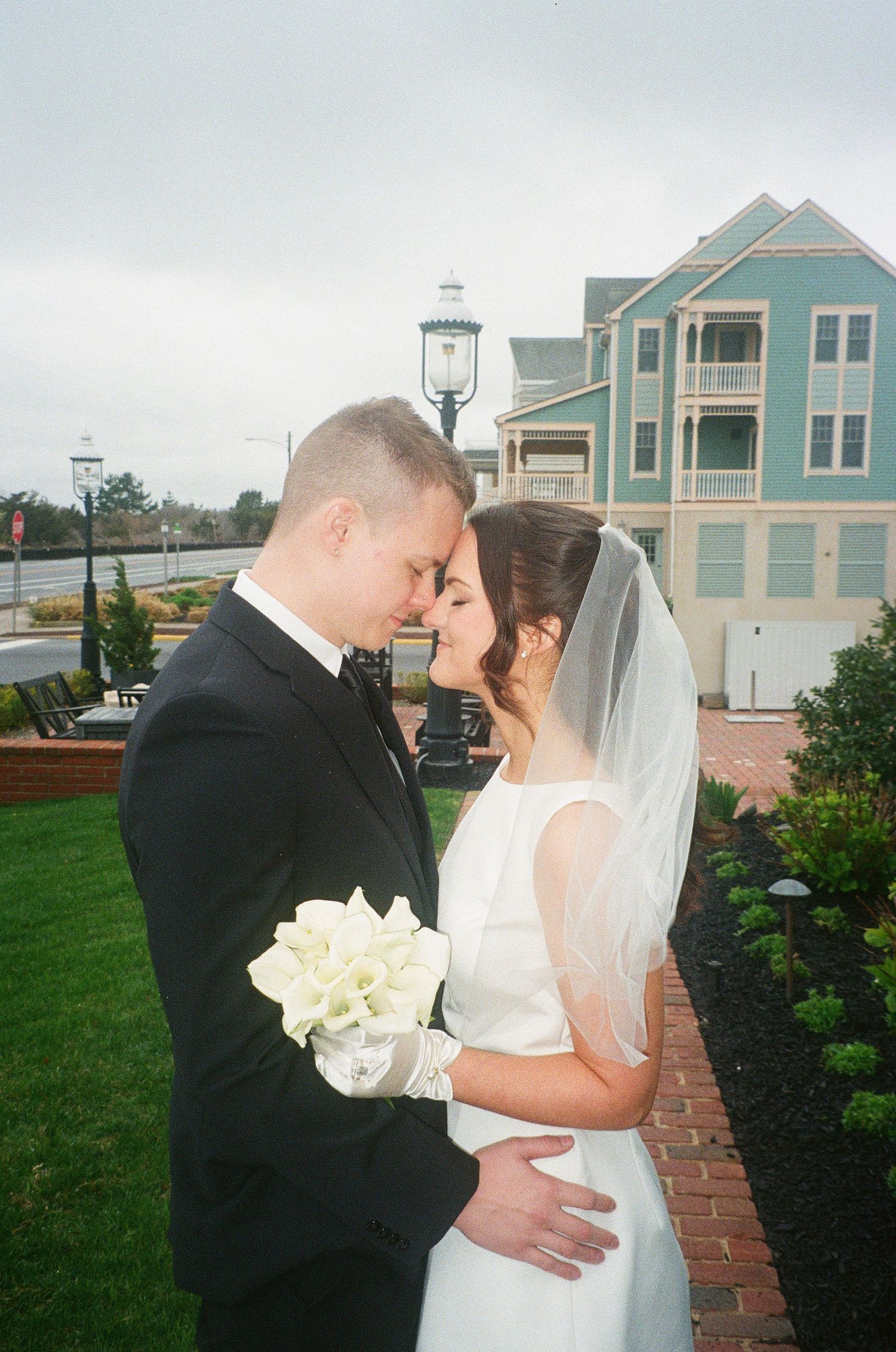 A romantic wedding photo with coastal buildings in the background on an overcast day.