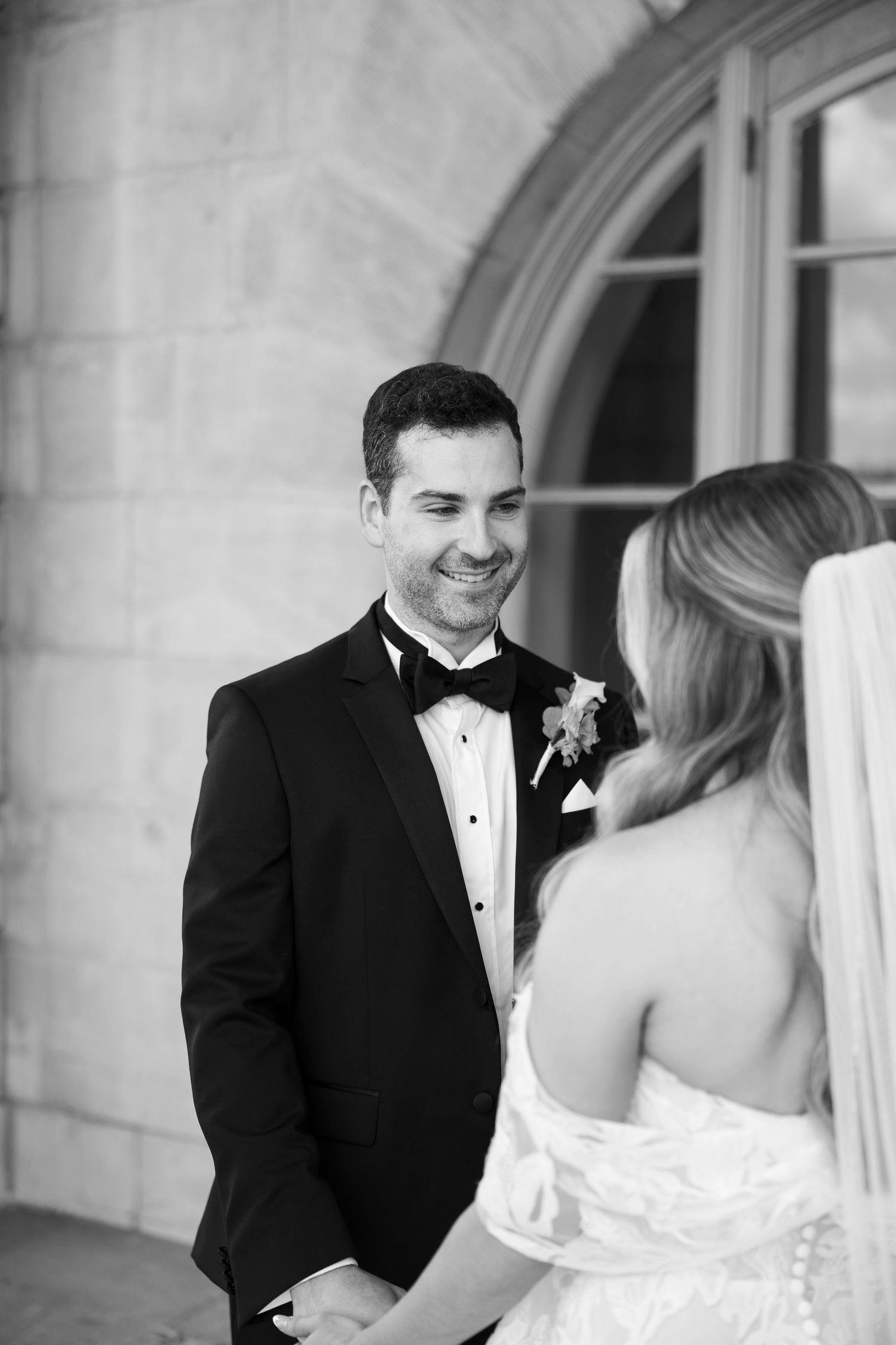 Black and white wedding photo capturing emotional first look reaction on stone terrace.