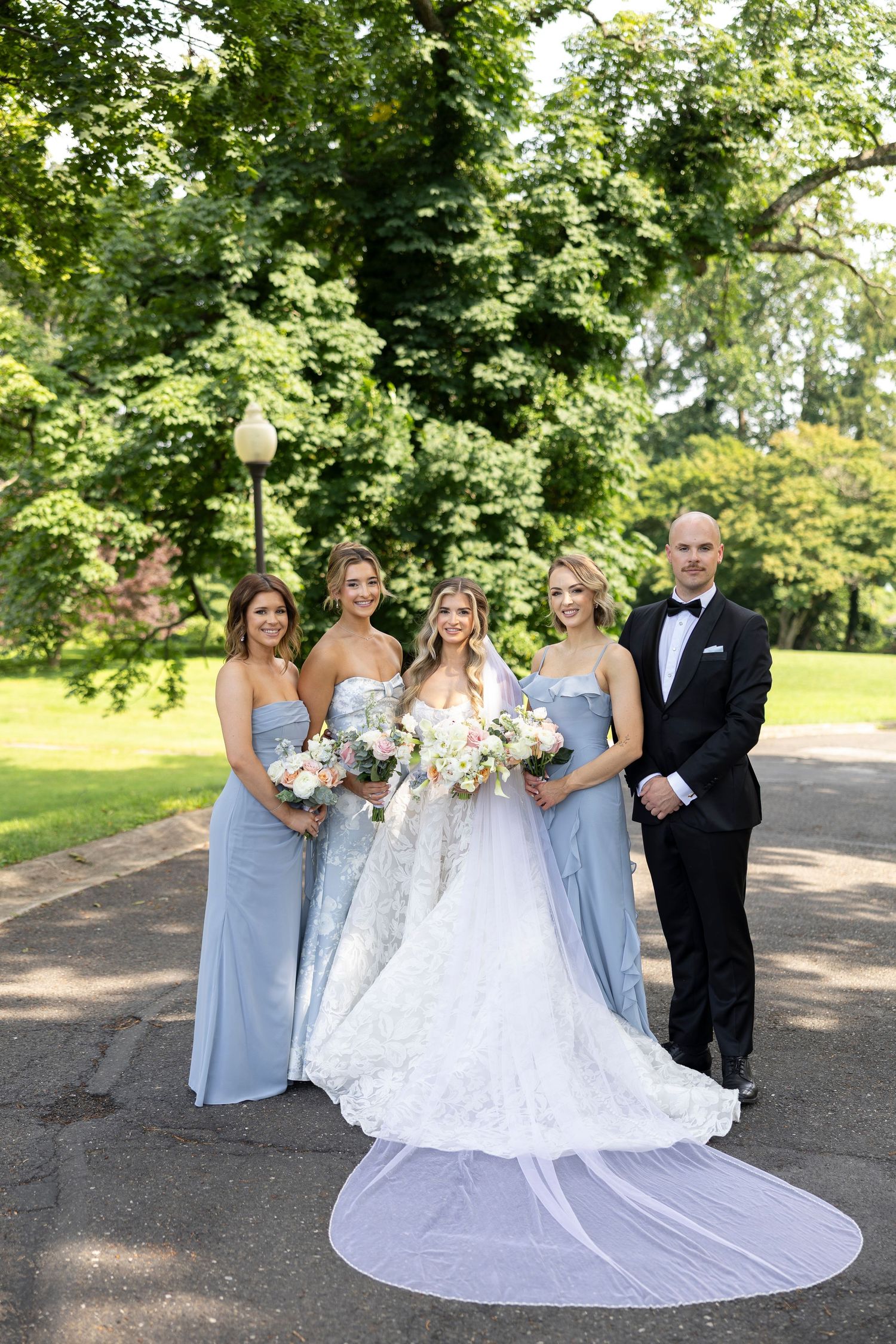 Wedding party in light blue and white formal attire posing together outdoors.