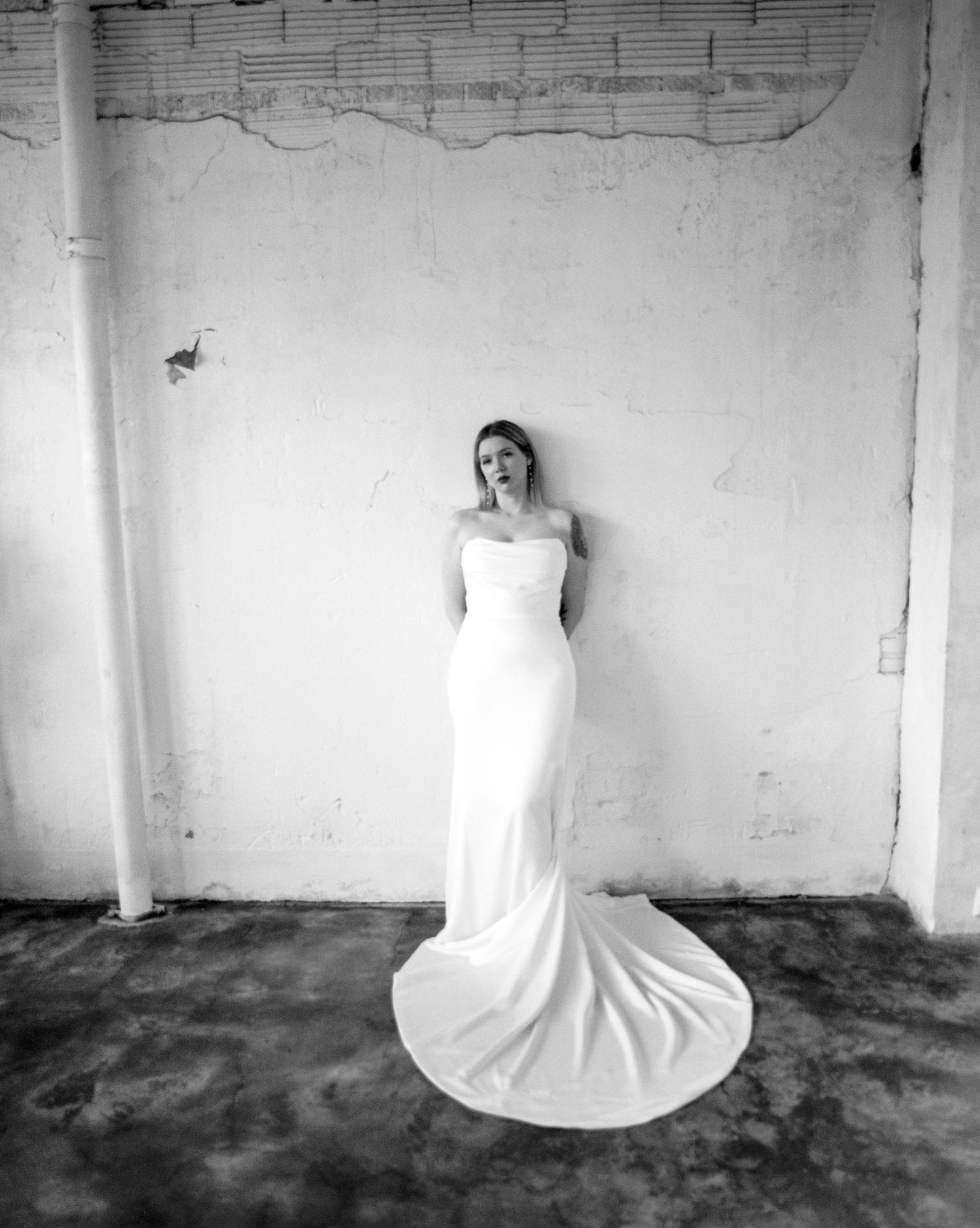 Black and white bridal portrait series showcasing elegant gown silhouette in industrial setting.
