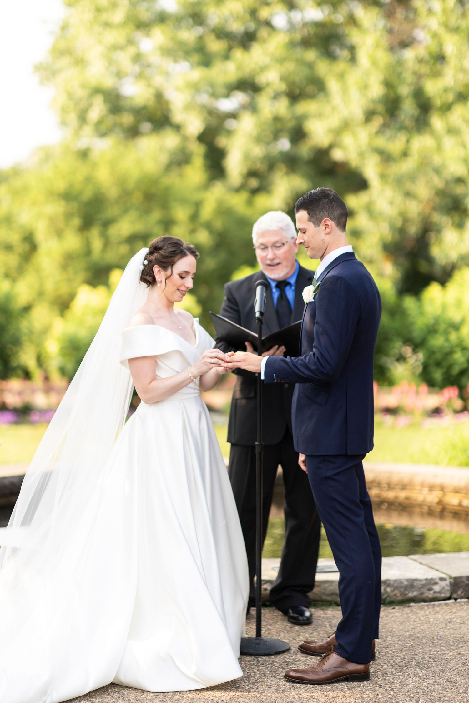 Intimate moment during wedding ceremony as couple exchanges rings in lush garden setting.