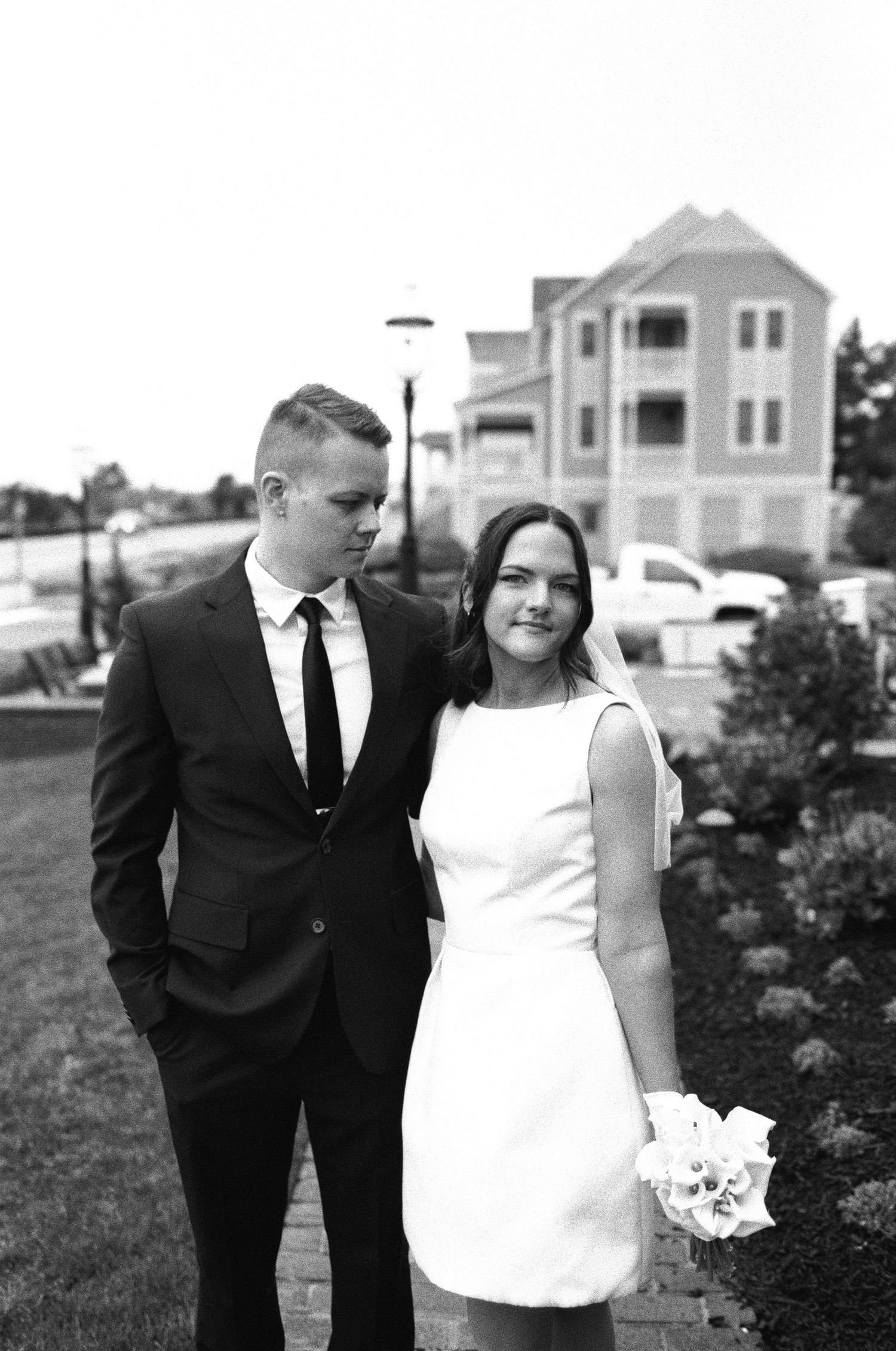 Wedding couple in classic black and white attire posing outdoors near beach houses.