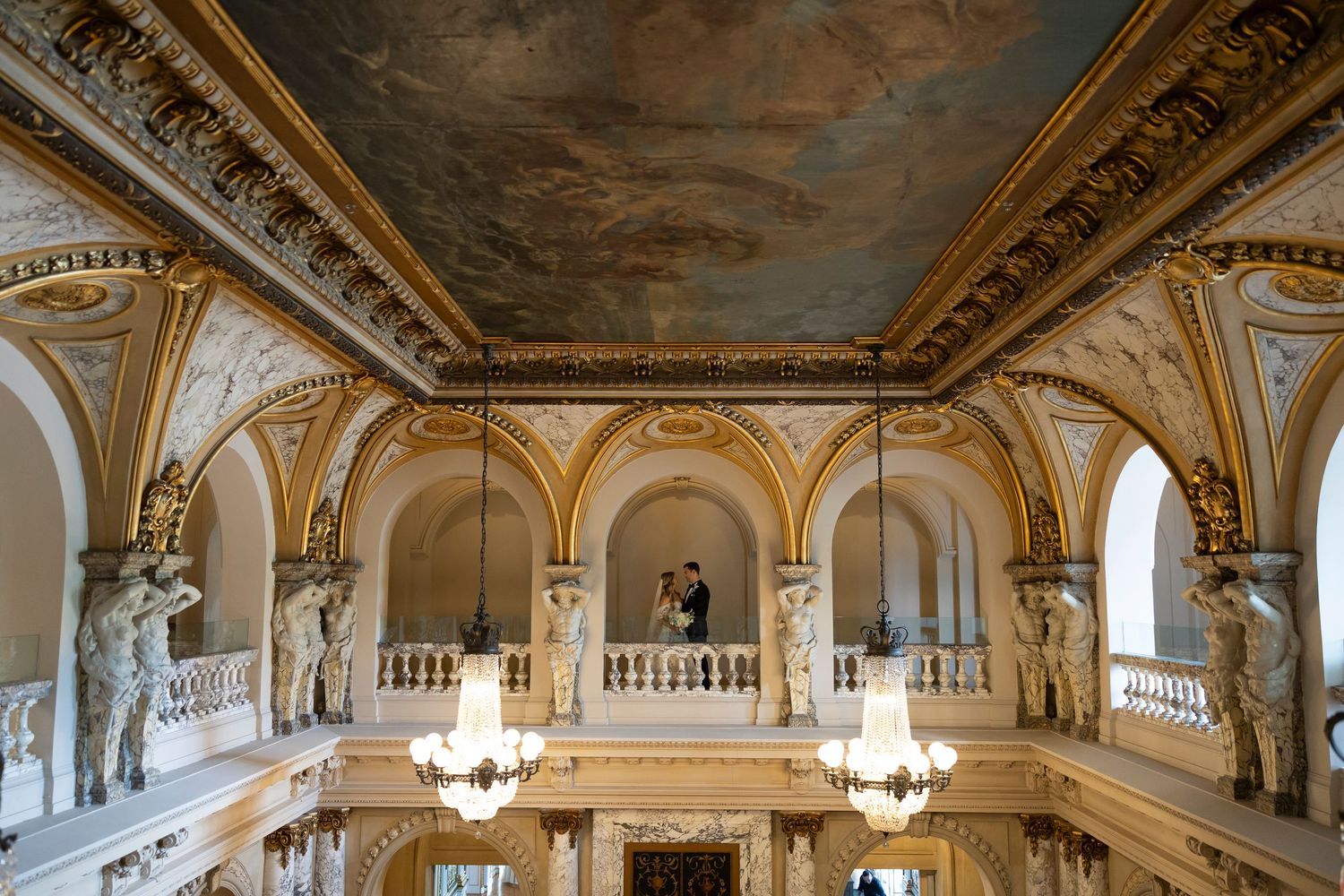 Ornate gilded ceiling with chandeliers in a grand ballroom setting.