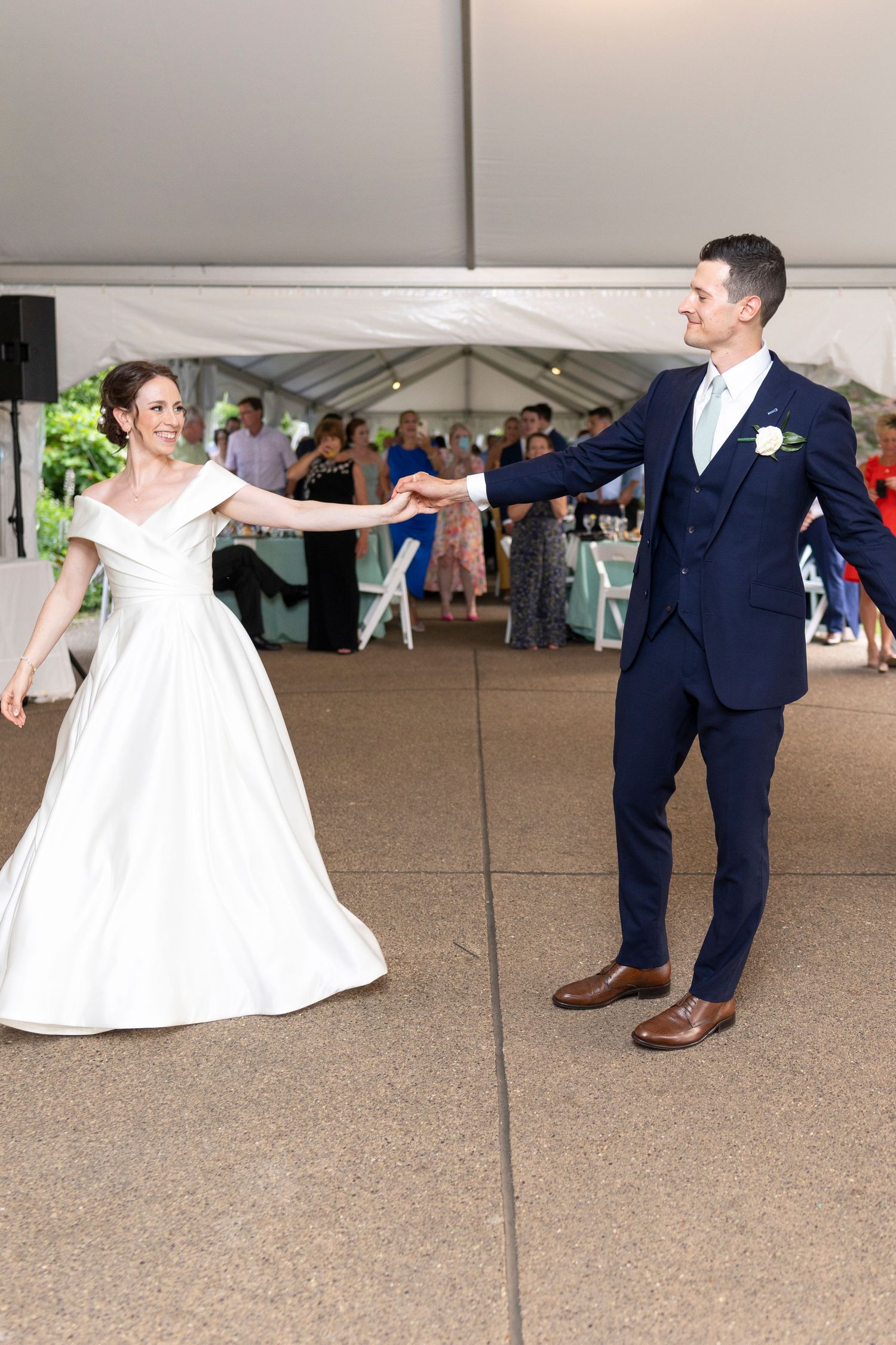 Newlyweds perform a playful dance move on their wedding day under a white tent.