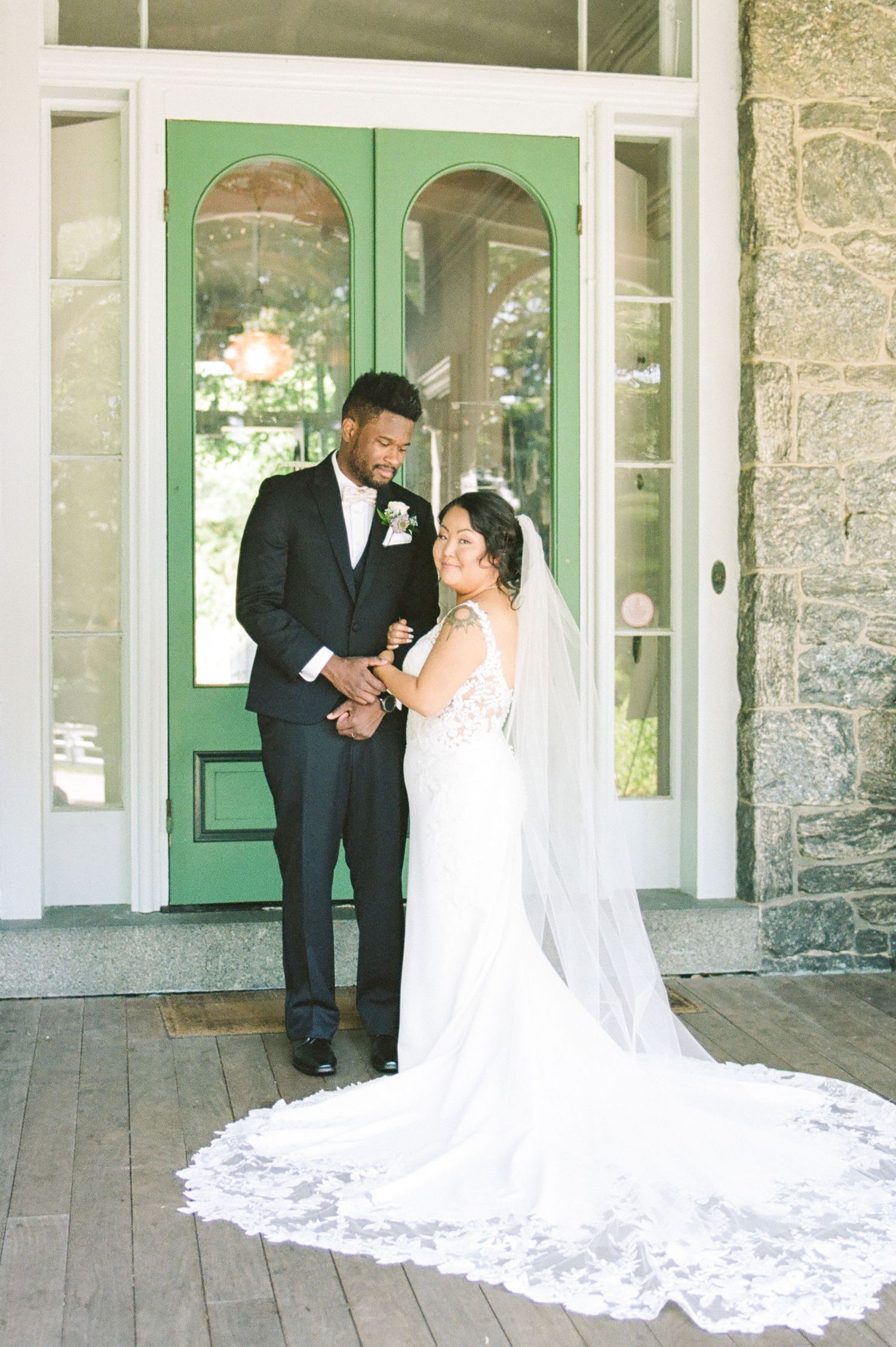 A romantic wedding moment on a stone porch with a flowing white veil and elegant attire.
