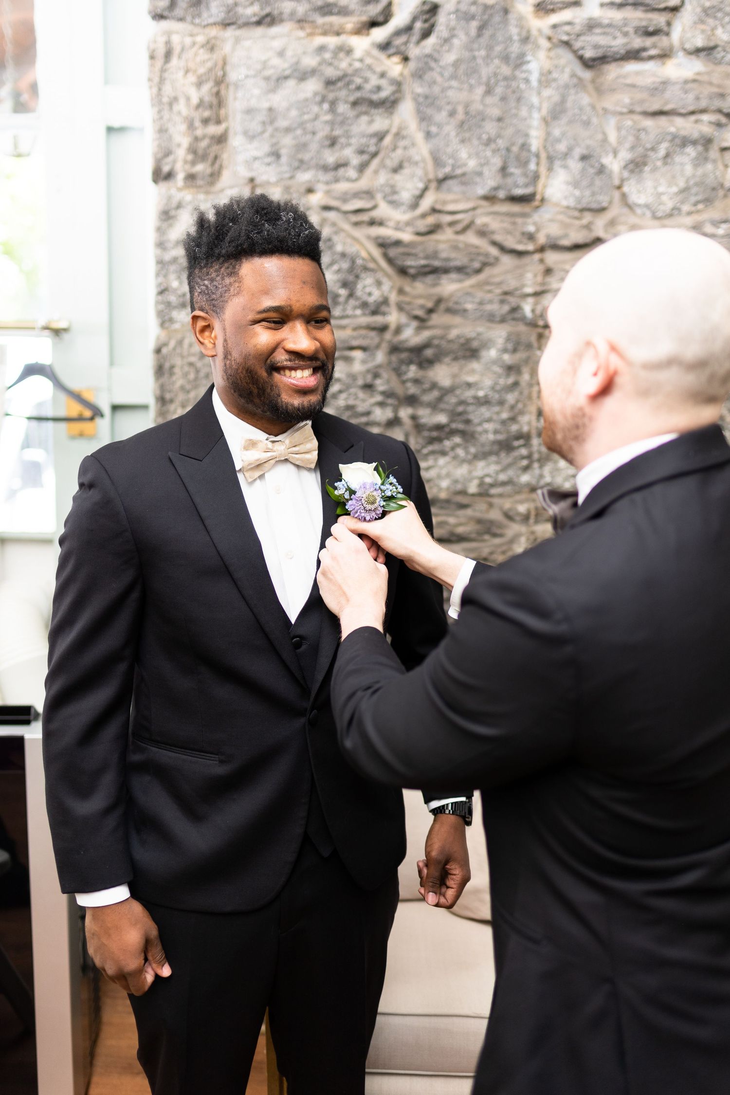 Two people in formal attire share a lighthearted moment while adjusting a tie.