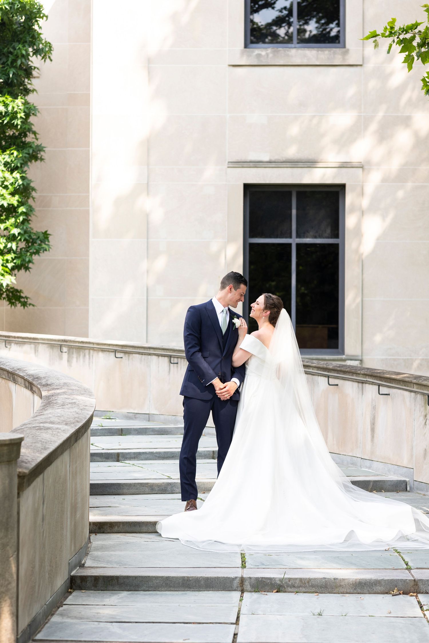Intimate wedding moment captured on stone steps with white building and windows in background.
