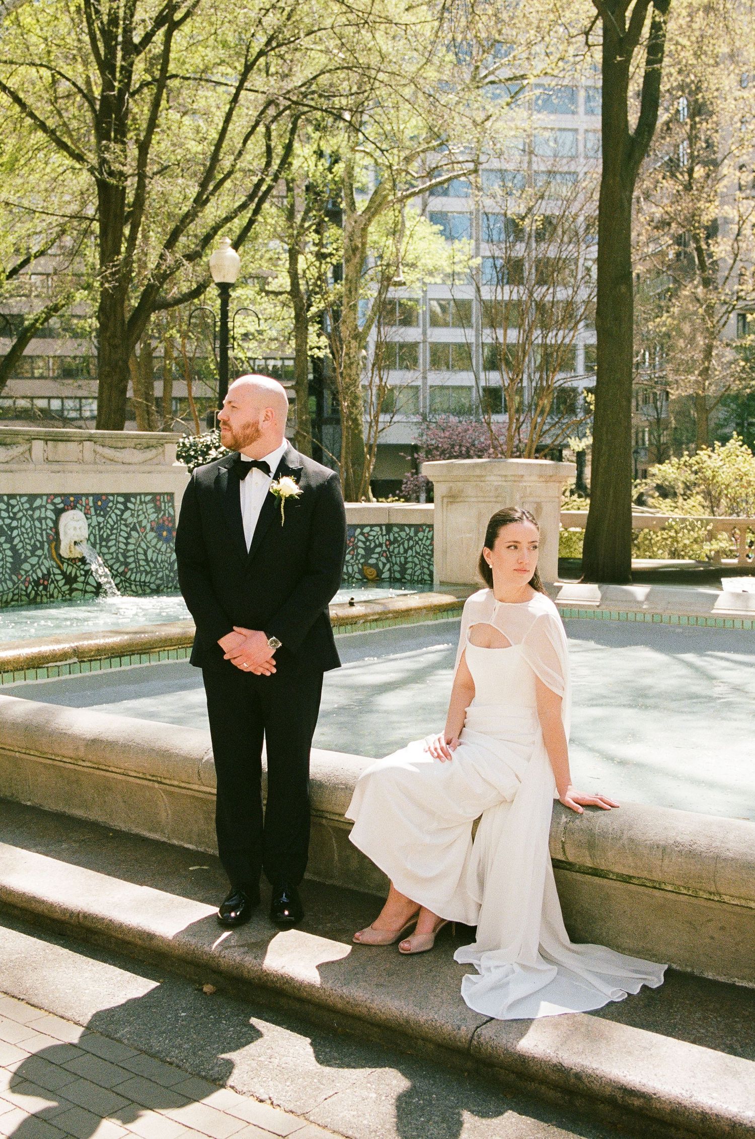 Bride and groom posing by a fountain in a park on their wedding day.