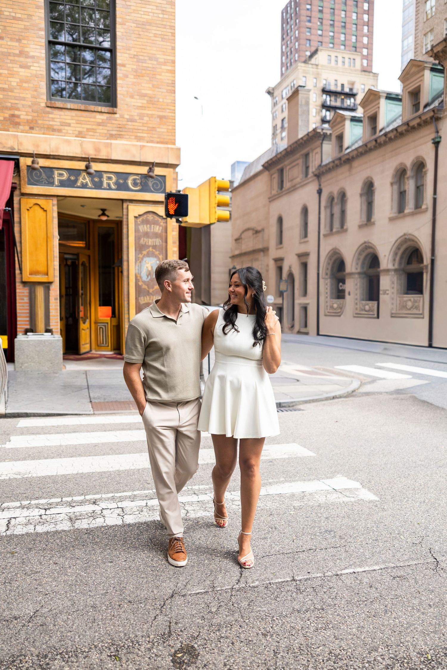 Couple walking hand in hand down a city street with brick buildings and traffic signs.