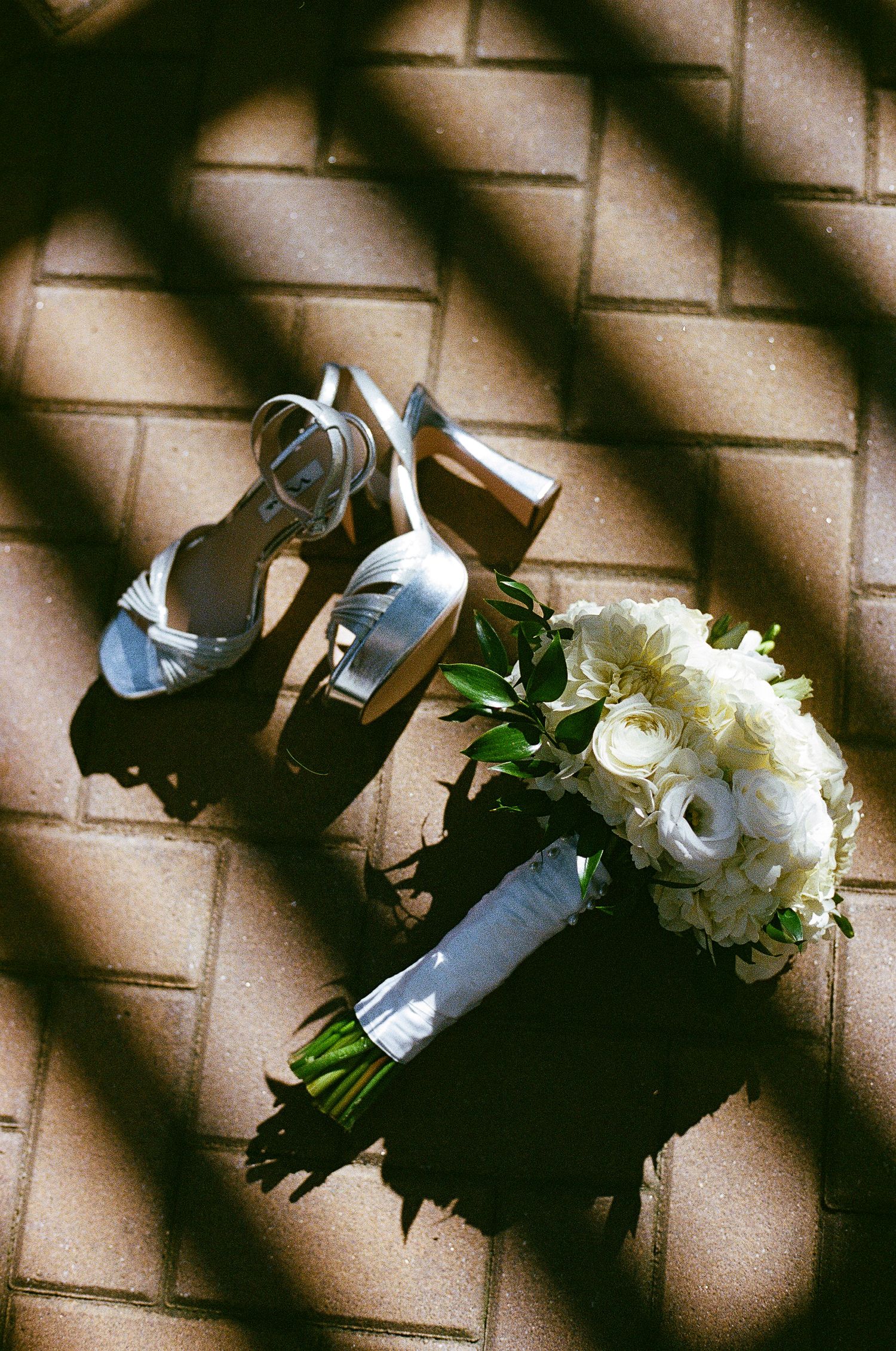 White floral bouquet and silver shoes casting dramatic shadows on textured floor.