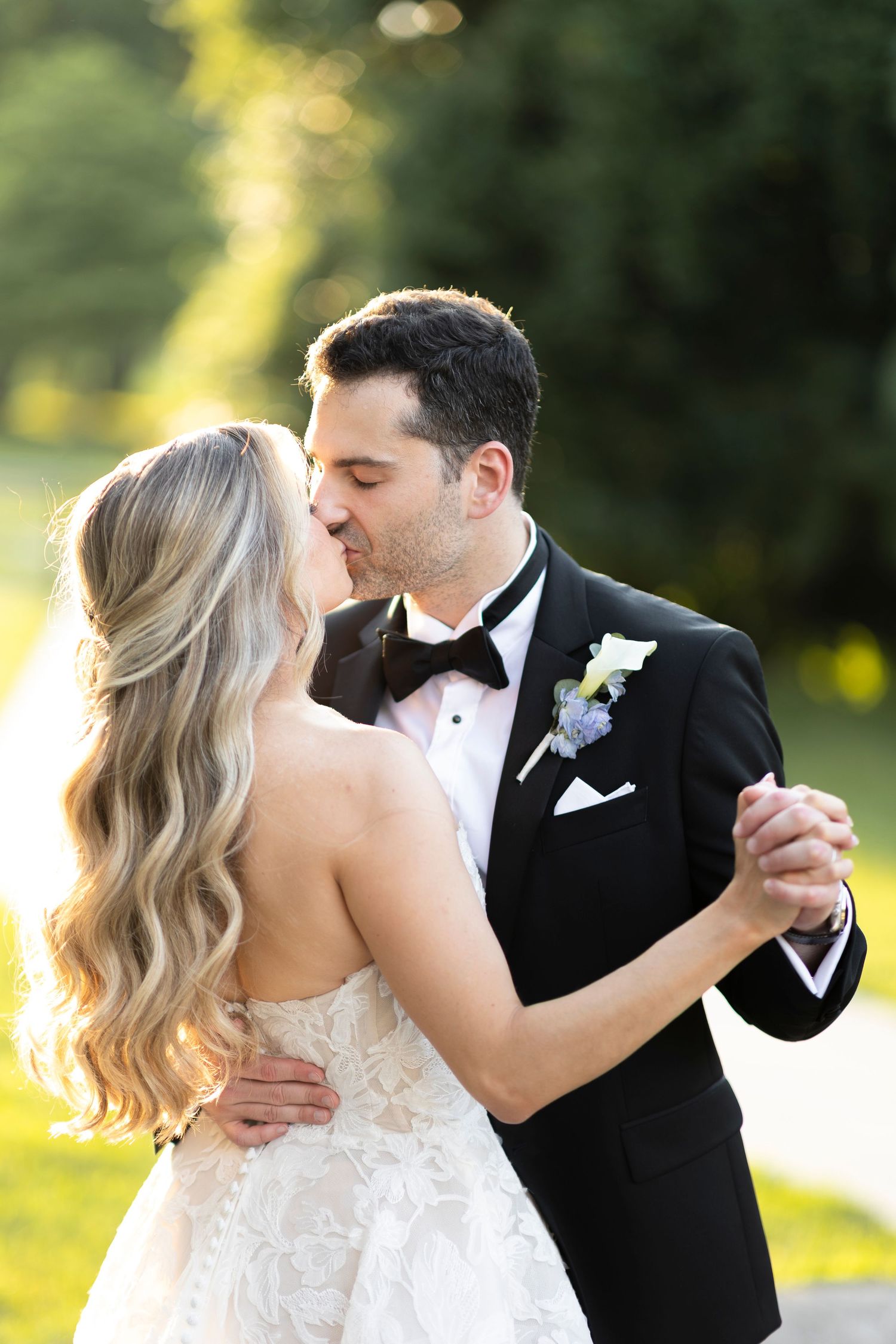 Elegant couple in wedding attire dances together in golden afternoon light.