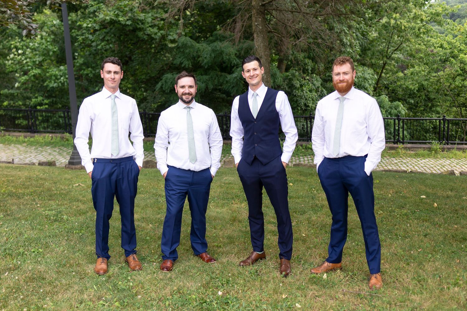 Groomsmen in navy suits and brown shoes pose casually on grass.