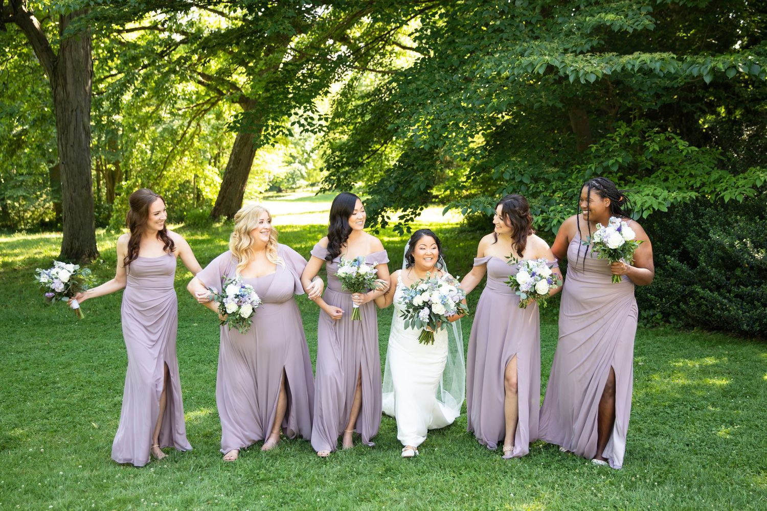 Wedding party members arranged in casual poses on grass under trees.