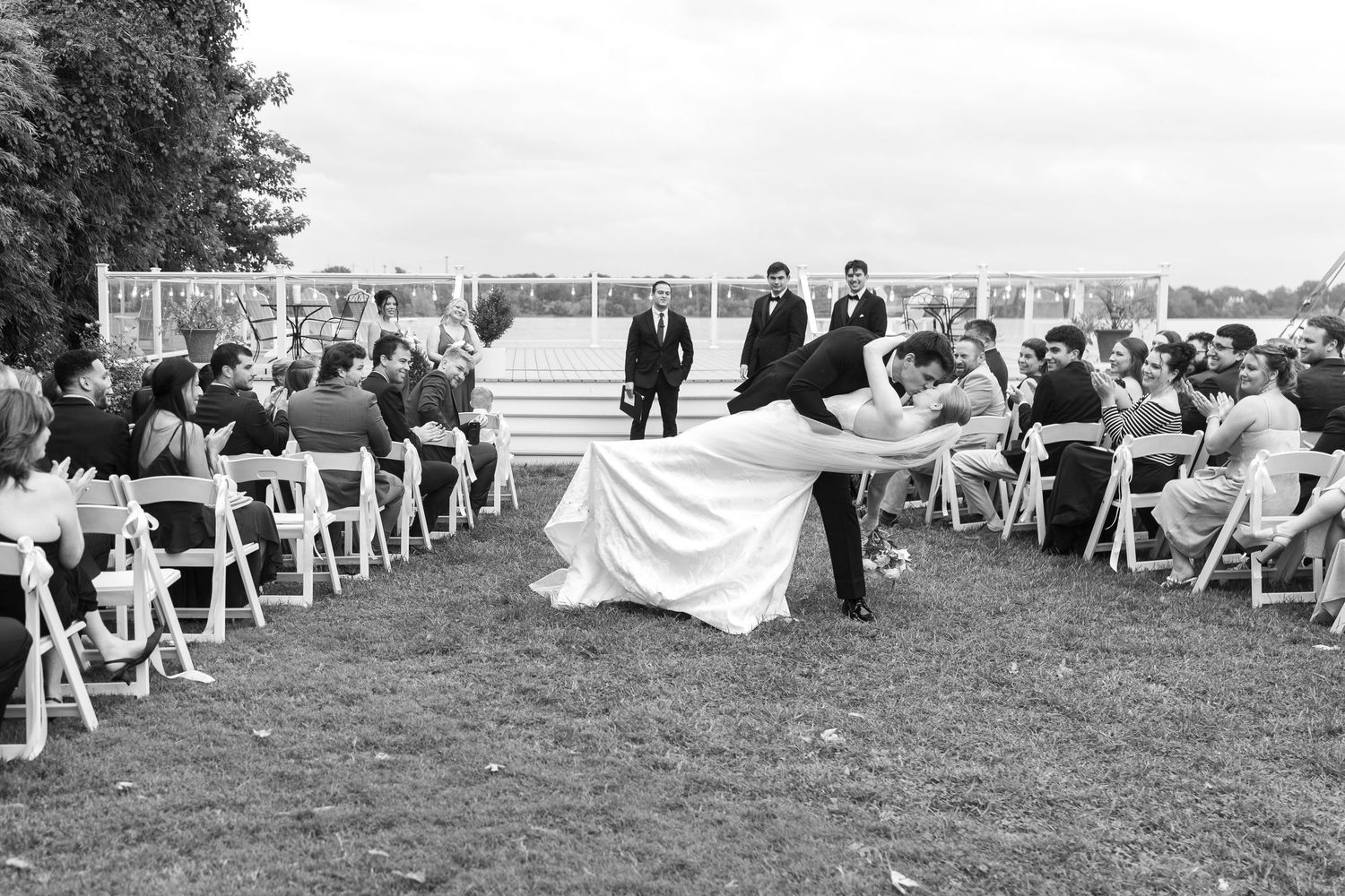 Panoramic view of outdoor wedding ceremony setup with white chairs and waterfront backdrop.