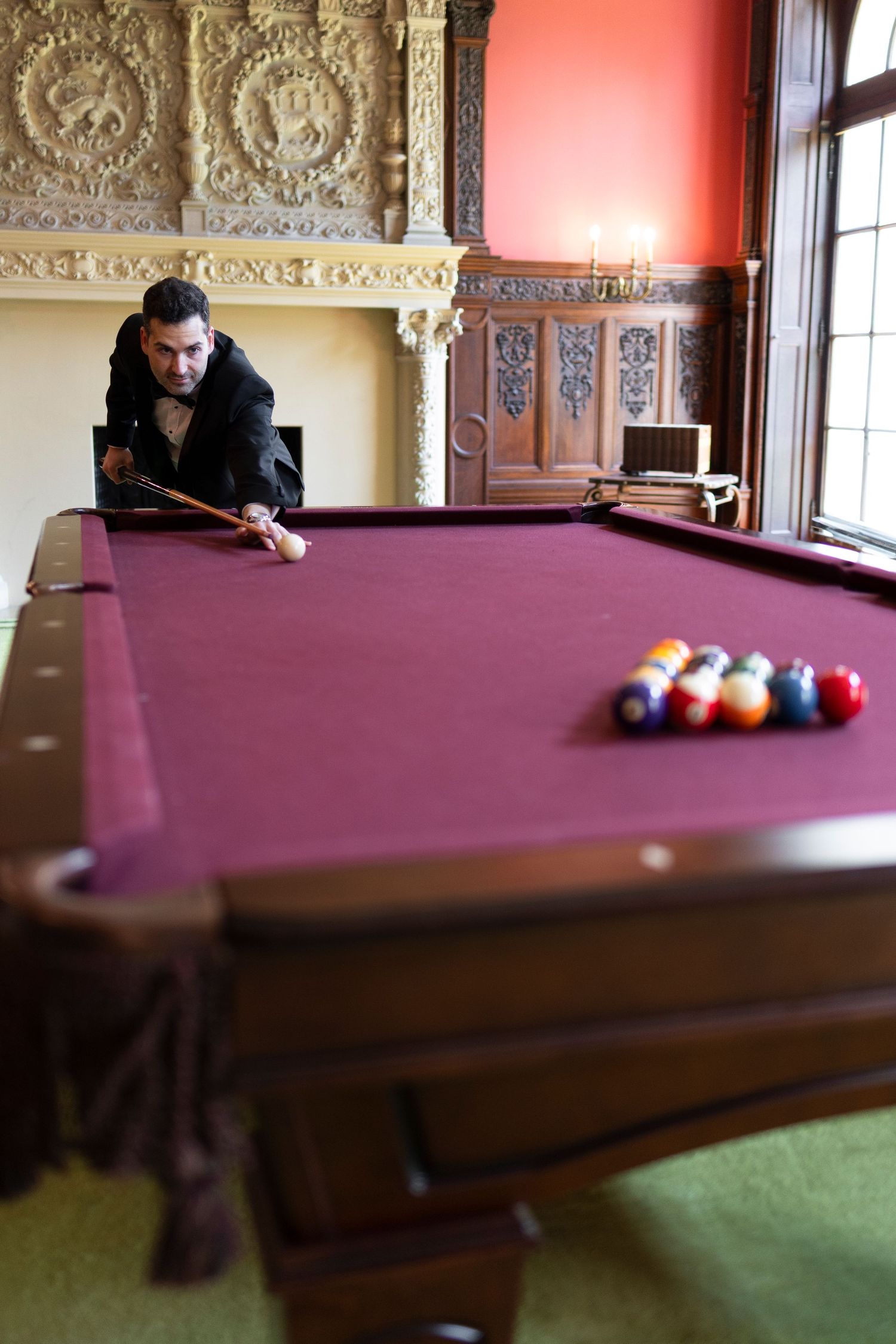 Pool table in an ornate room with decorative moldings and red walls.