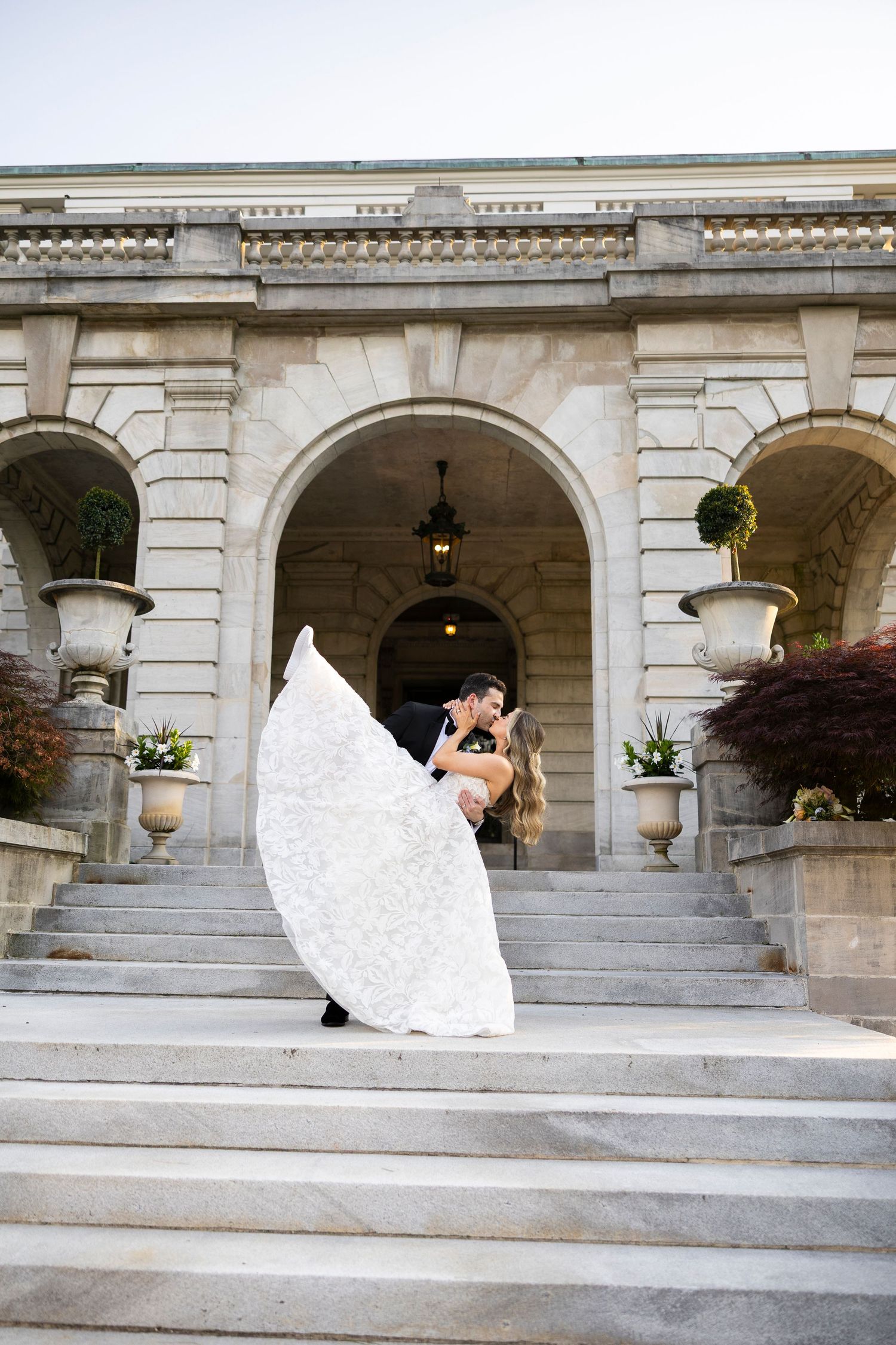 Wedding couple poses dramatically on grand stone steps of a classical building.