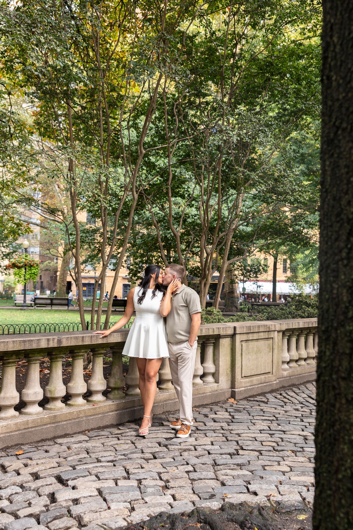 Couple poses together on a stone balustrade walkway in an urban park setting.