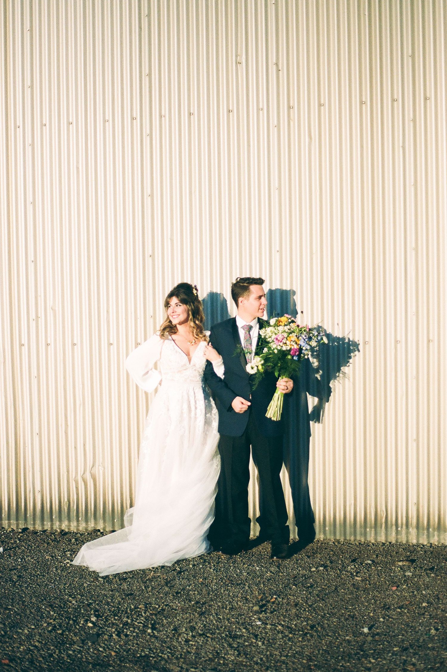 Wedding party posing against corrugated metal wall in dramatic lighting.