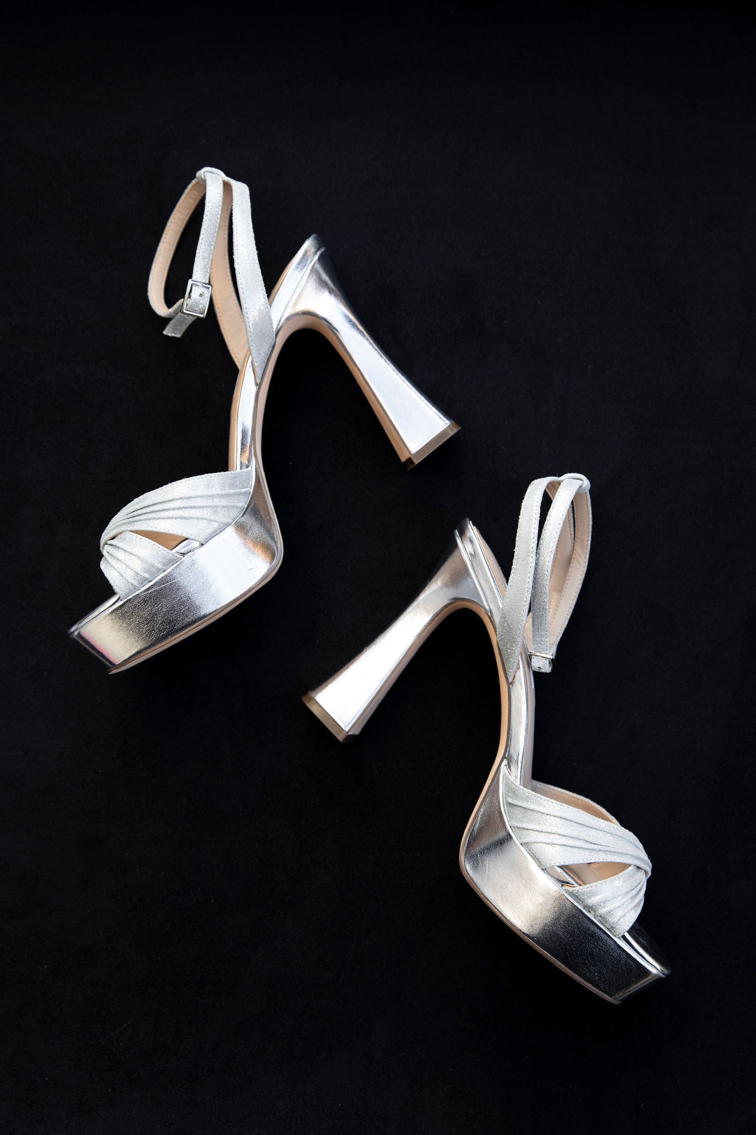 Silver metallic high heel shoes floating on black background.