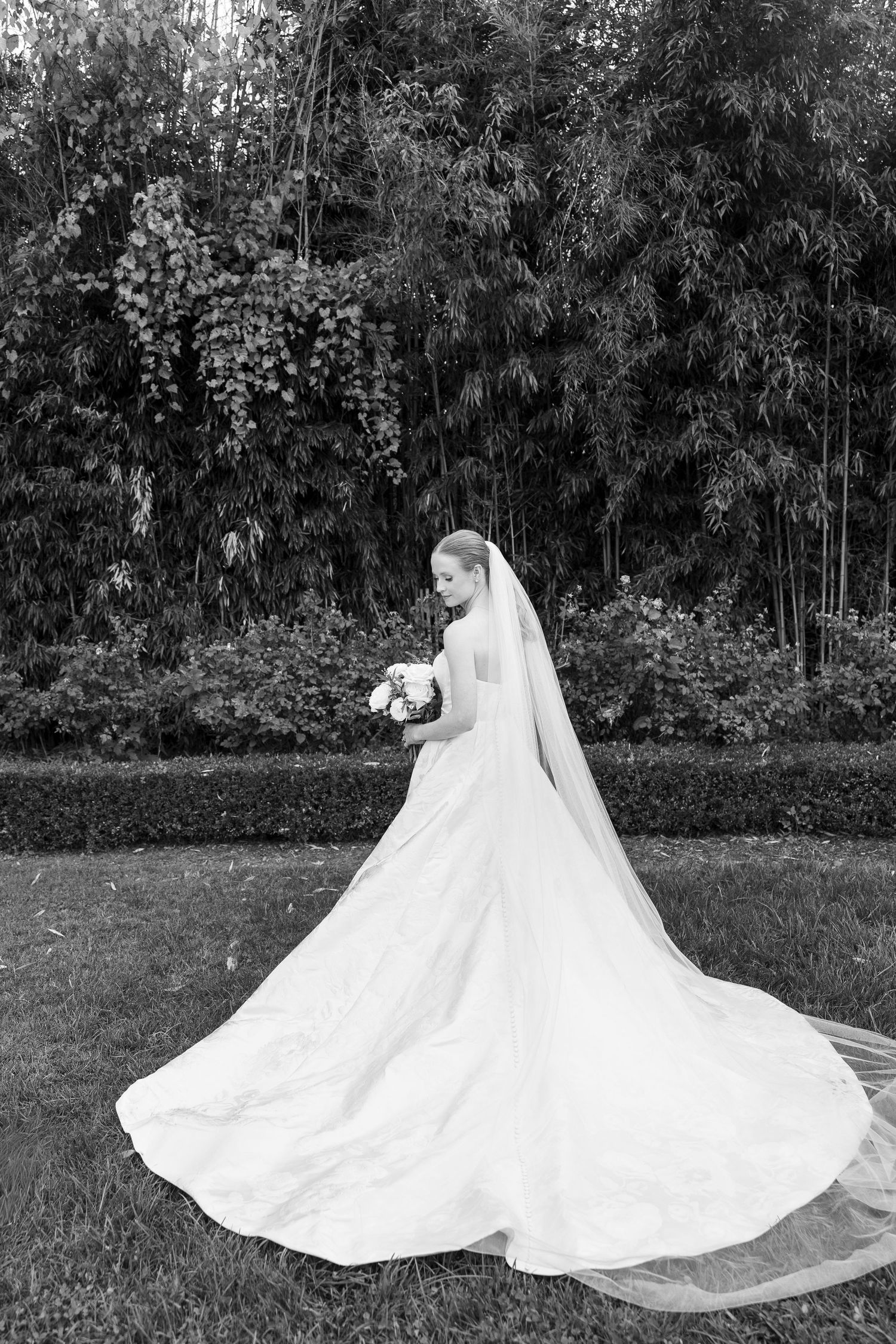 A flowing white wedding dress with a long train twirls gracefully in a garden setting.