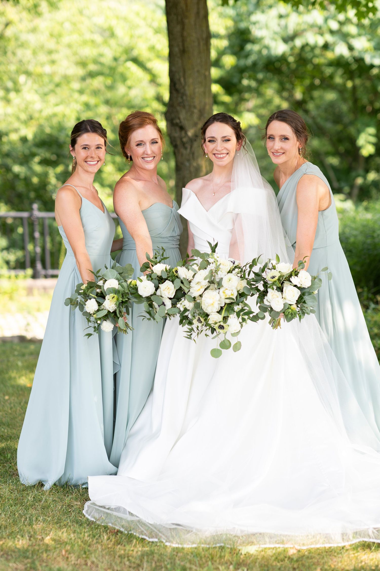 Bridesmaids in light blue dresses hold white floral bouquets next to bride in white gown.